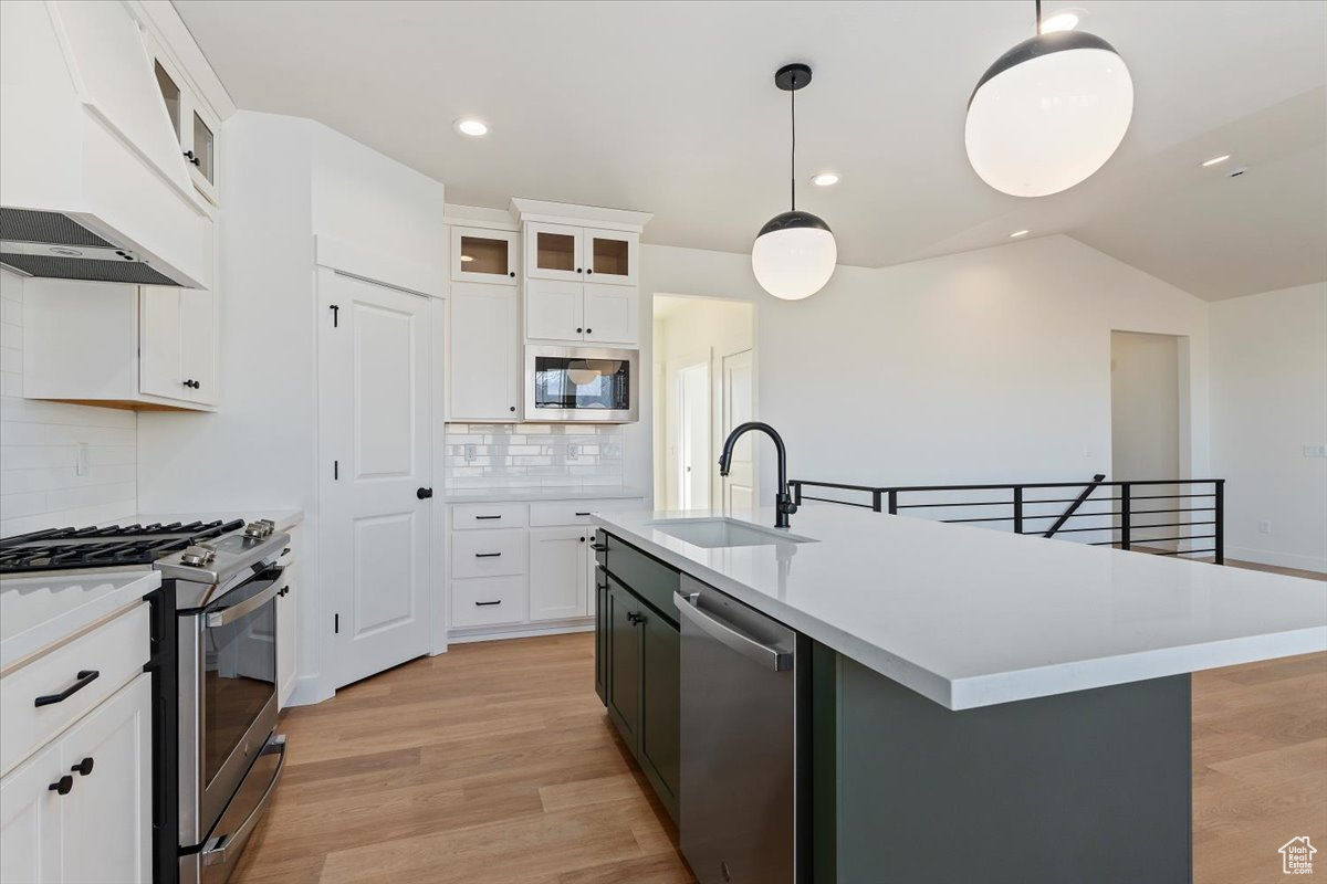 Kitchen with stainless steel gas range, exhaust hood, white cabinets, and designer light fixtures