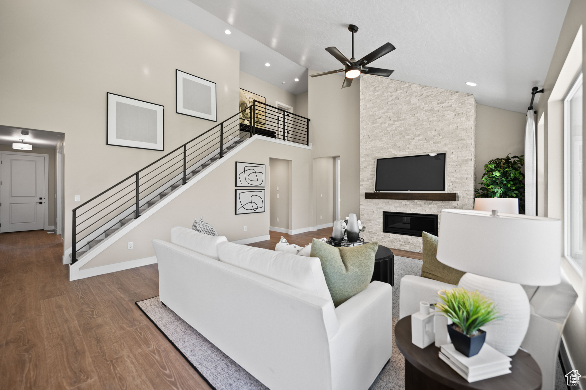 Living room with a high ceiling, a stone fireplace, ceiling fan, and wood-type flooring