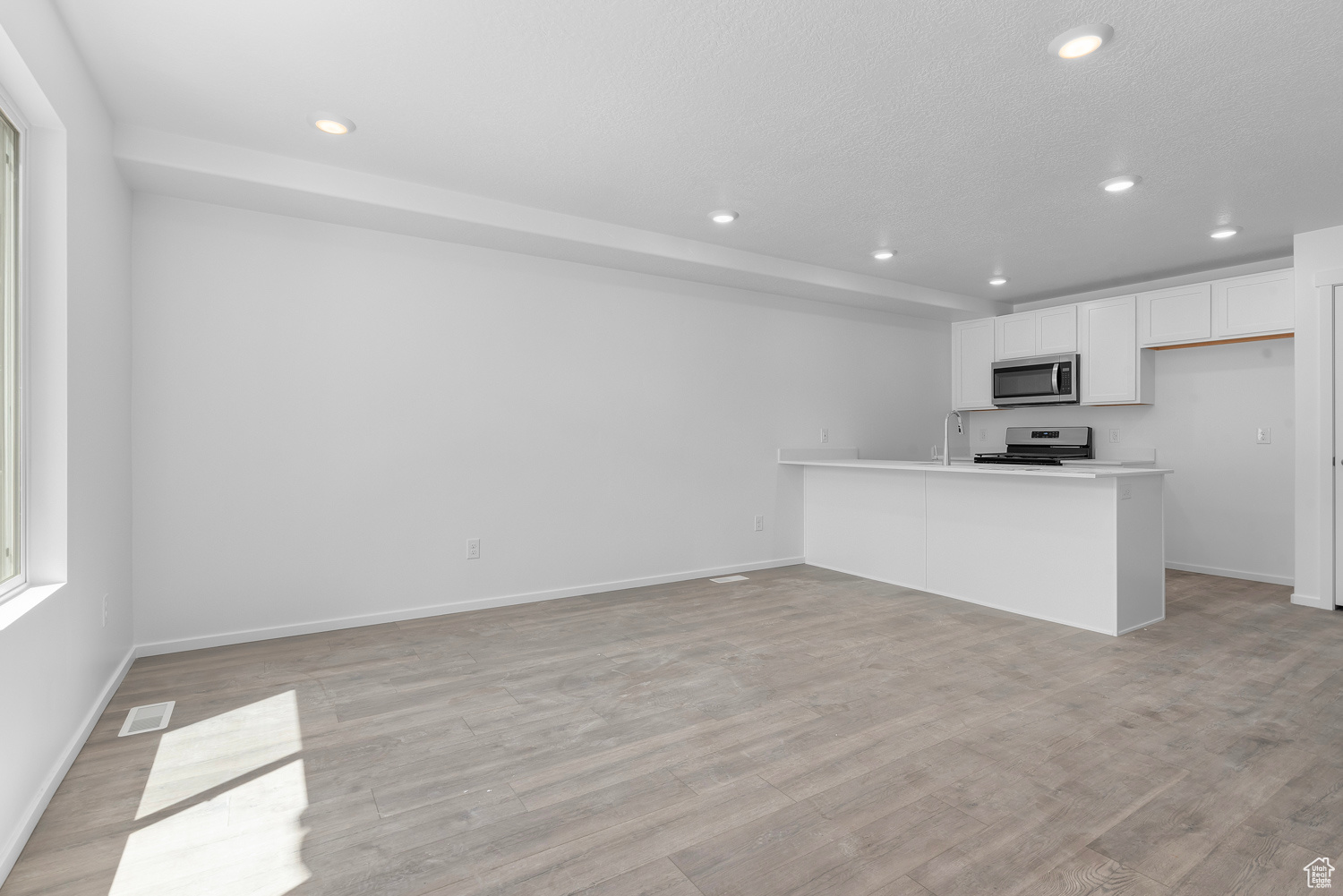 Kitchen with white cabinets, sink, appliances with stainless steel finishes, laminate flooring, and kitchen peninsula