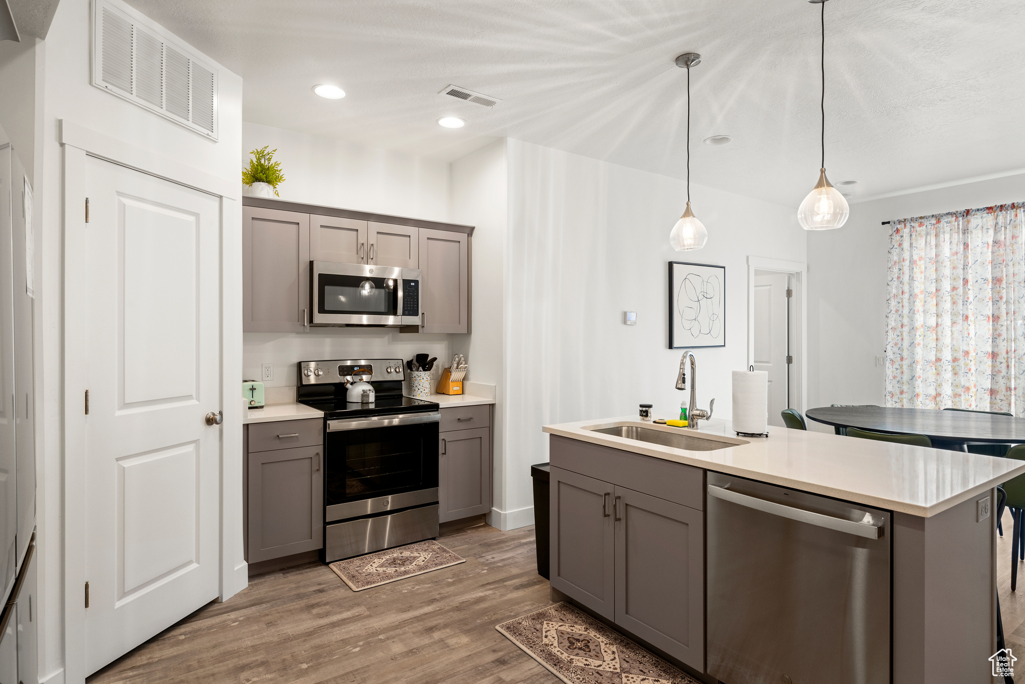 Kitchen with gray cabinetry, a center island with sink, sink, appliances with stainless steel finishes, and decorative light fixtures