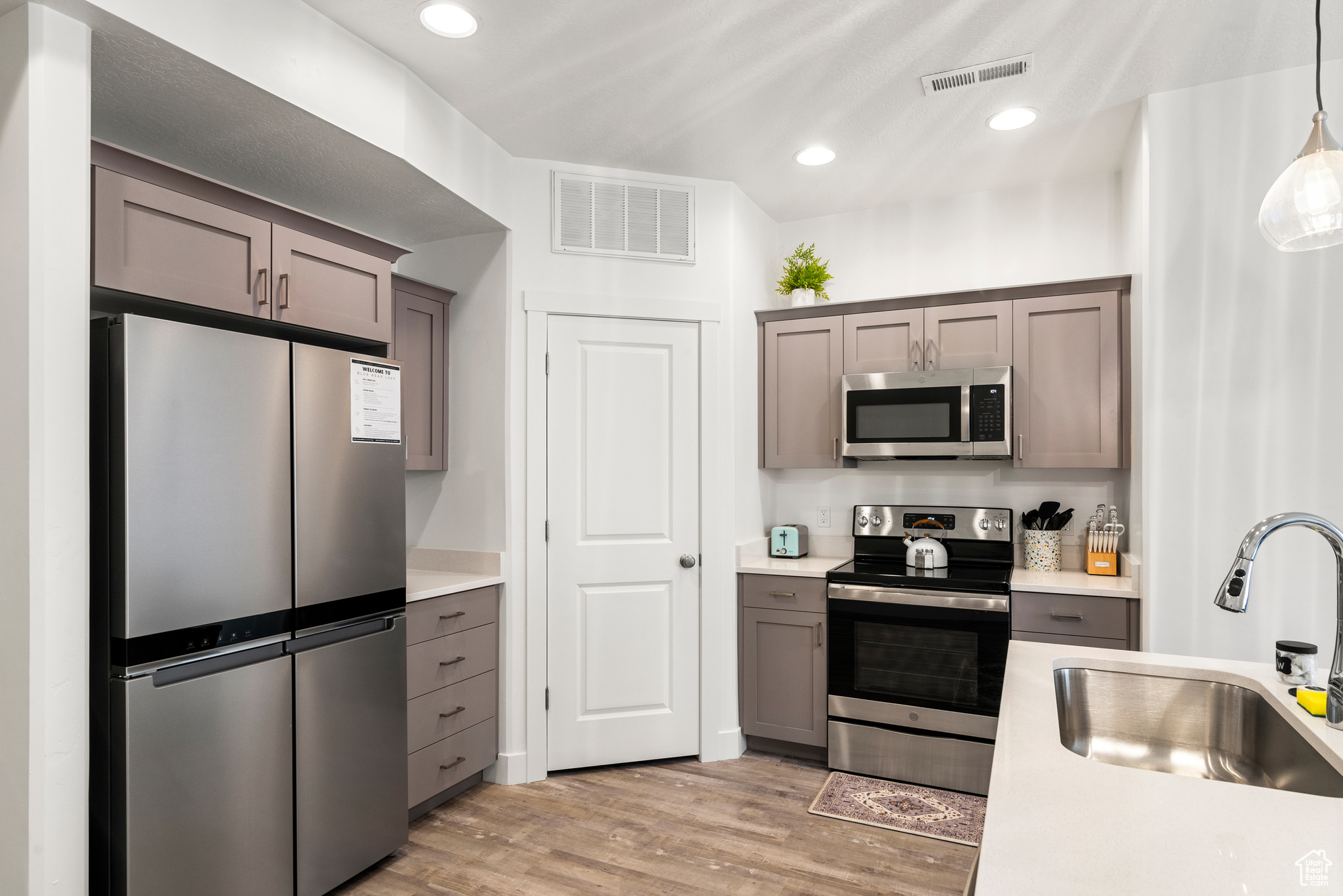 Kitchen with pendant lighting, stainless steel appliances, light hardwood / wood-style floors, and sink