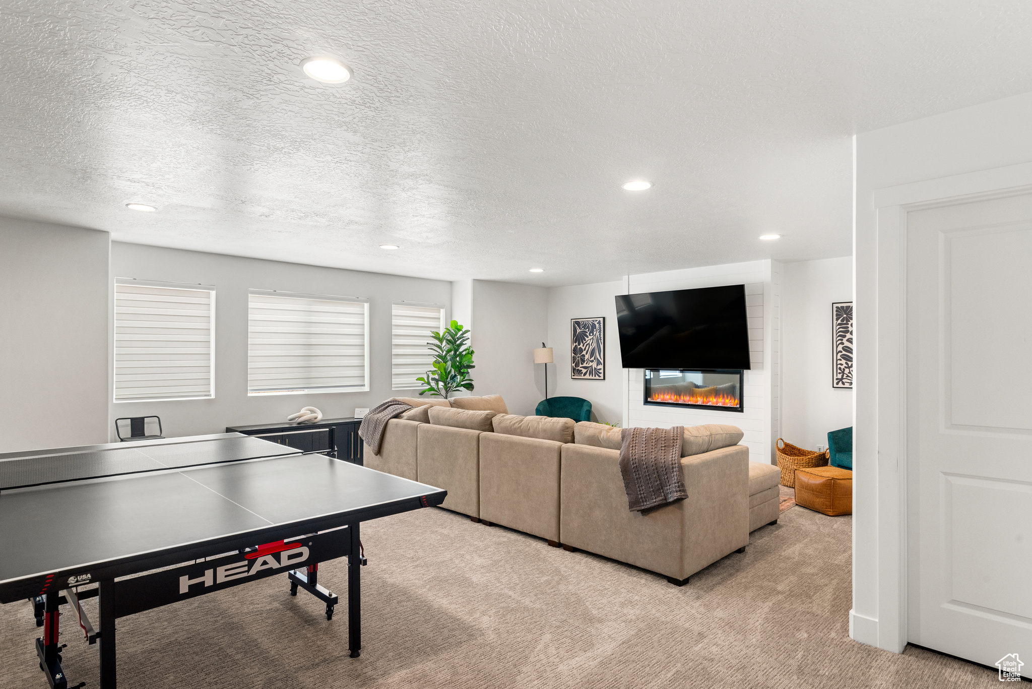 Game room with a large fireplace, light colored carpet, and a textured ceiling