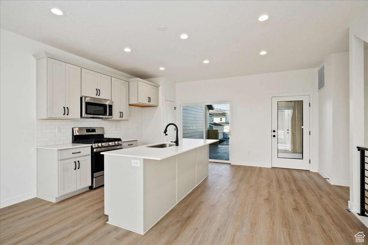 Kitchen featuring a kitchen island with sink, sink, white cabinets, and stainless steel appliances