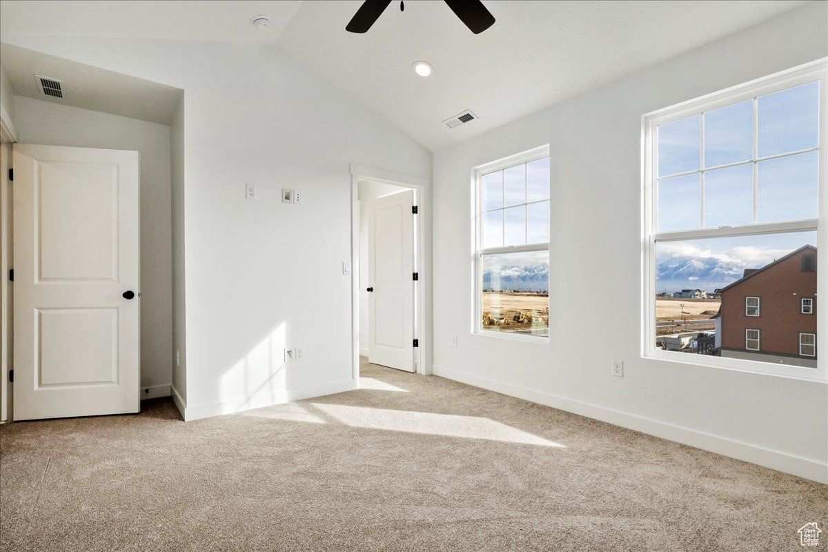 Spare room featuring light colored carpet, vaulted ceiling, and ceiling fan