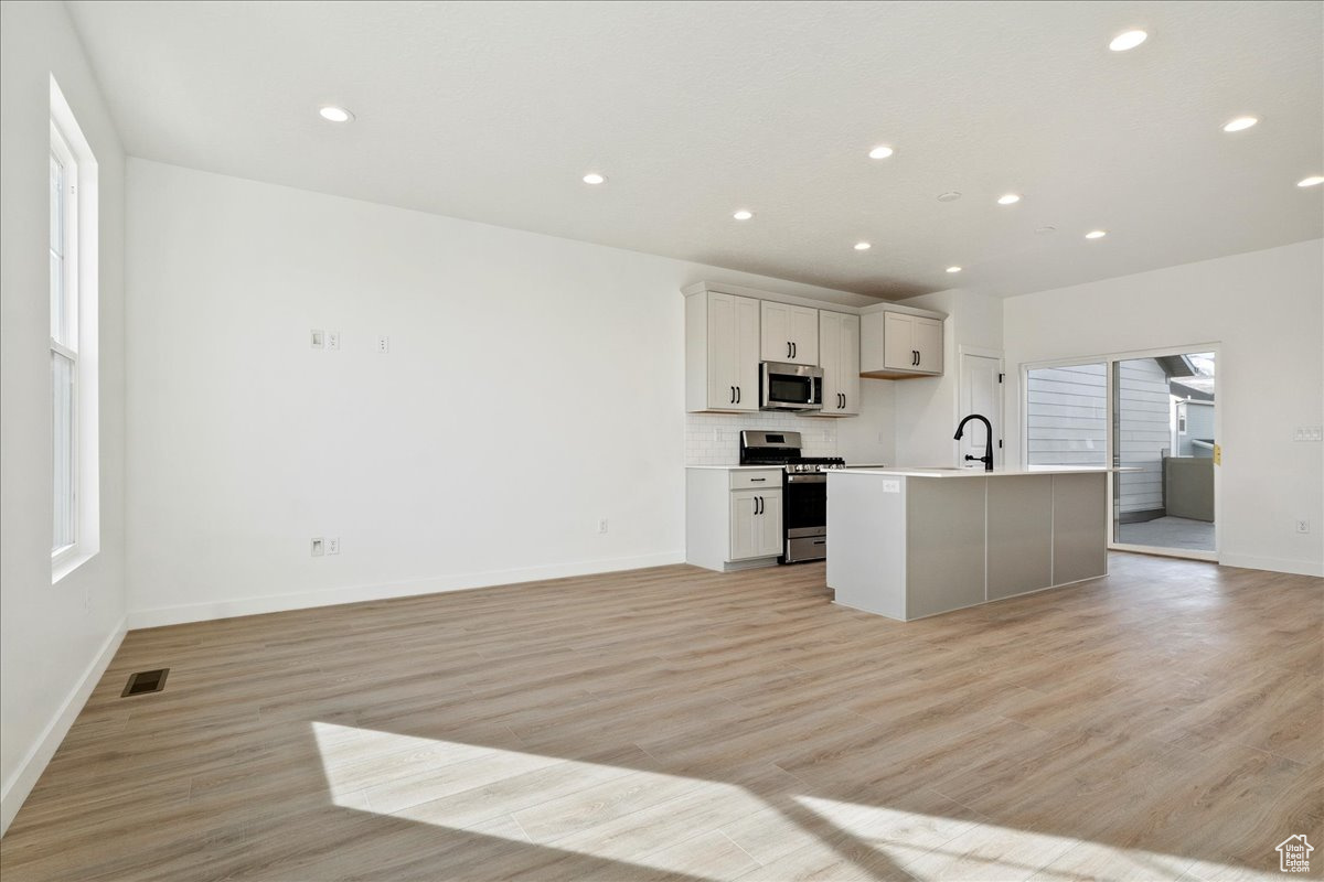 Kitchen with white cabinets, light wood-type flooring, stainless steel appliances, and a kitchen island with sink