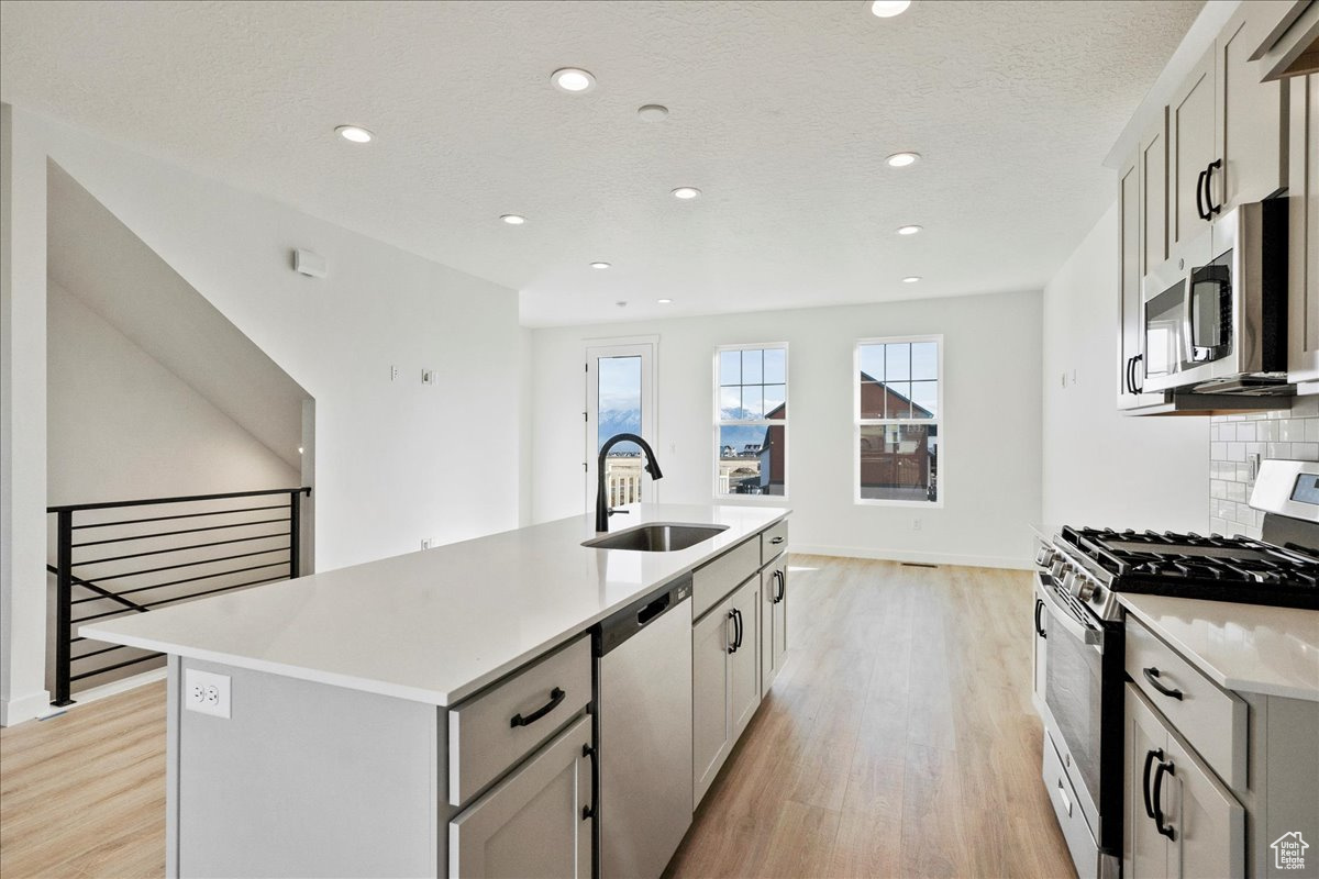 Kitchen featuring gray cabinetry, a center island with sink, sink, decorative backsplash, and stainless steel appliances