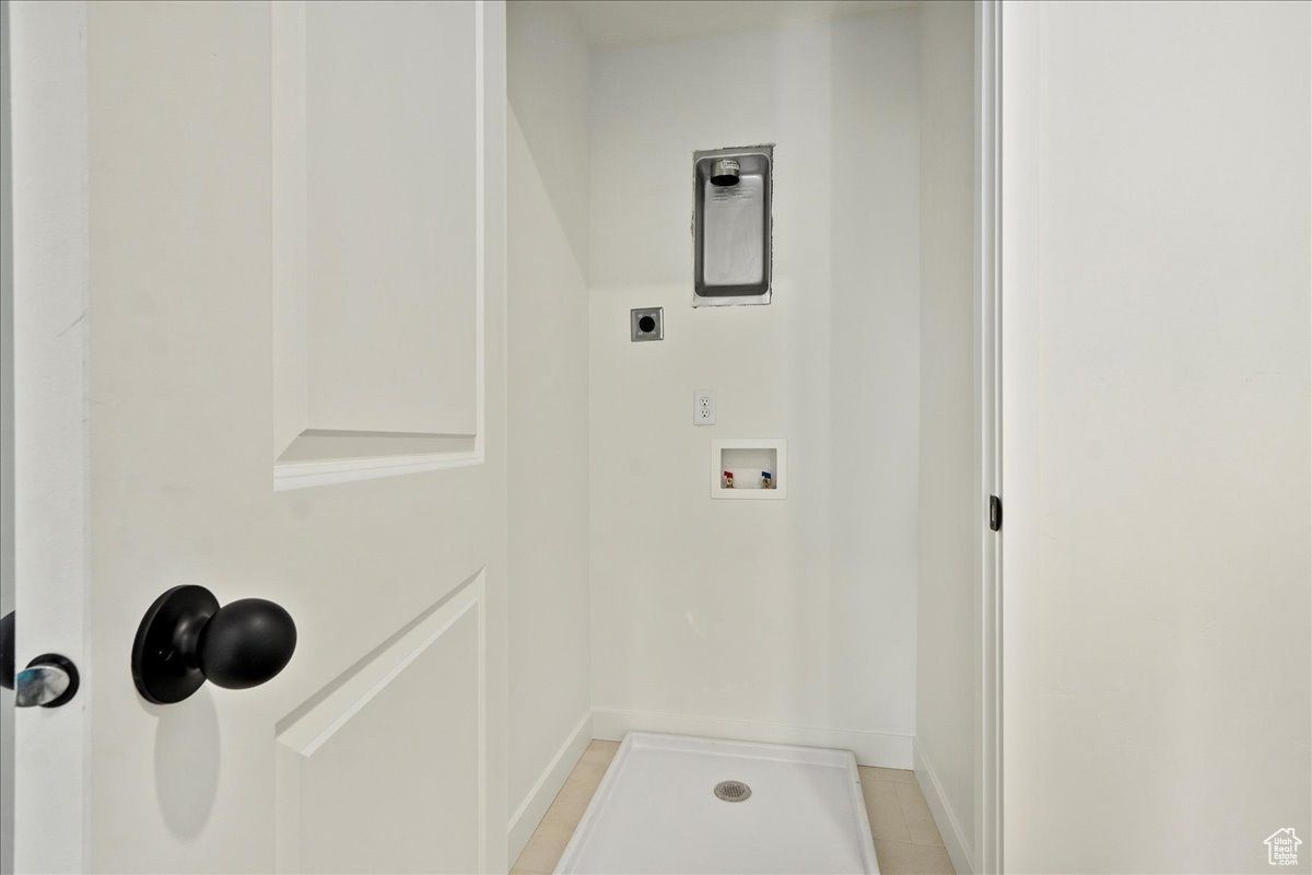 Laundry area with hookup for an electric dryer, light tile patterned flooring, and washer hookup