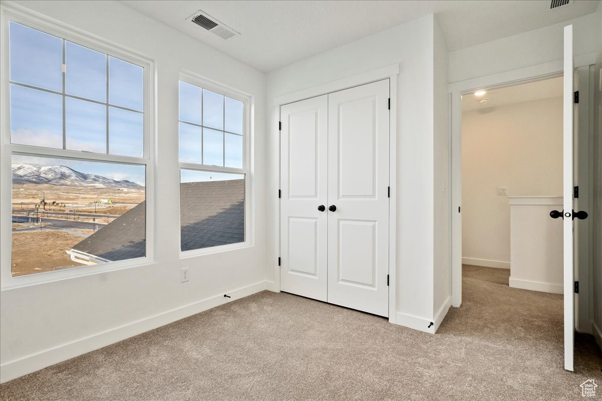 Unfurnished bedroom with a mountain view, light colored carpet, and a closet