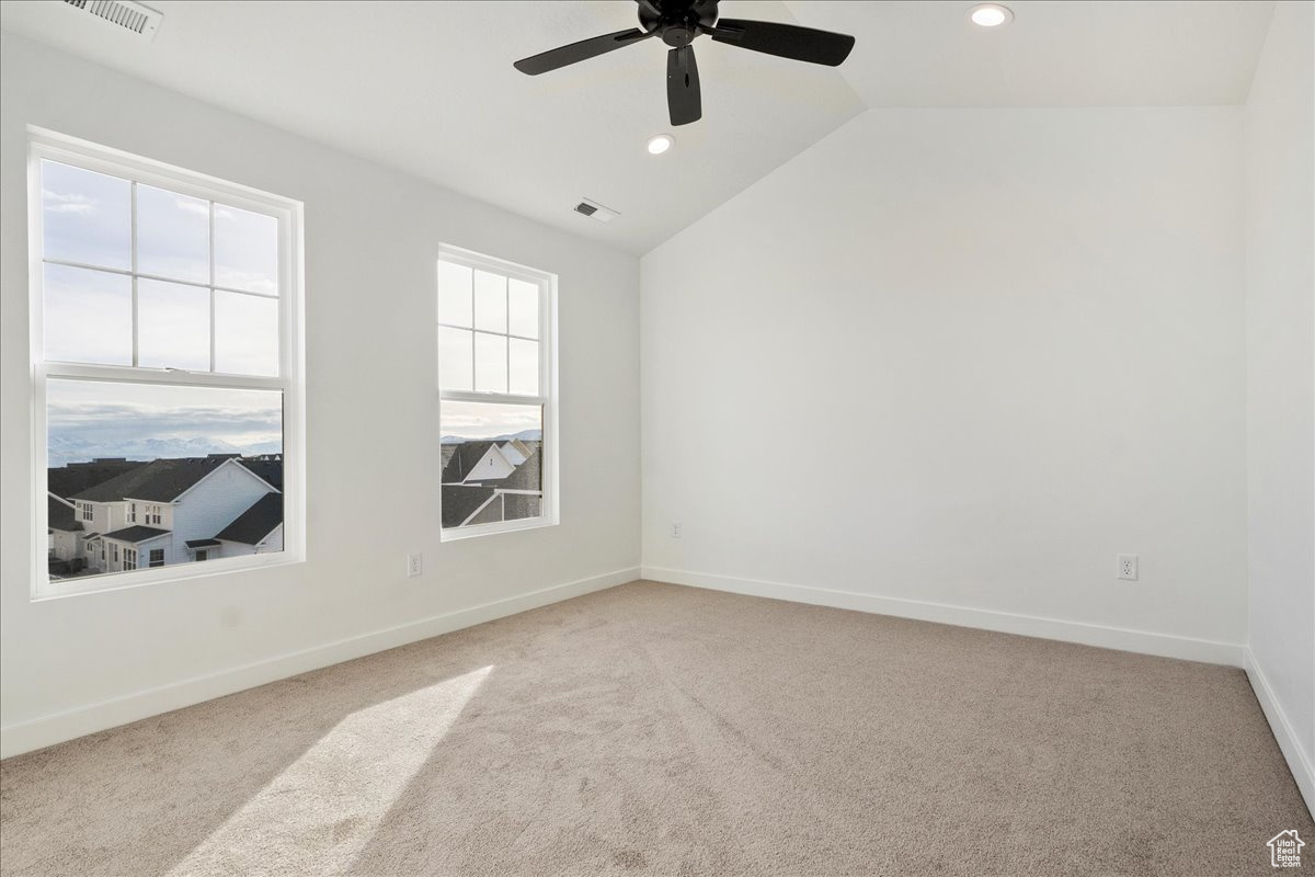 Carpeted empty room featuring vaulted ceiling and ceiling fan