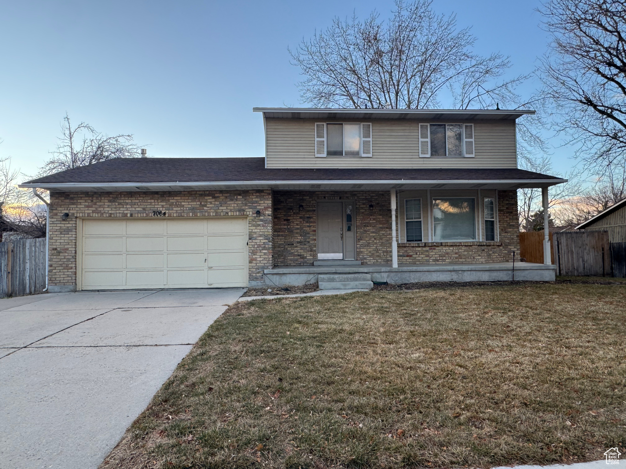 View of property with a porch, a garage, and a lawn