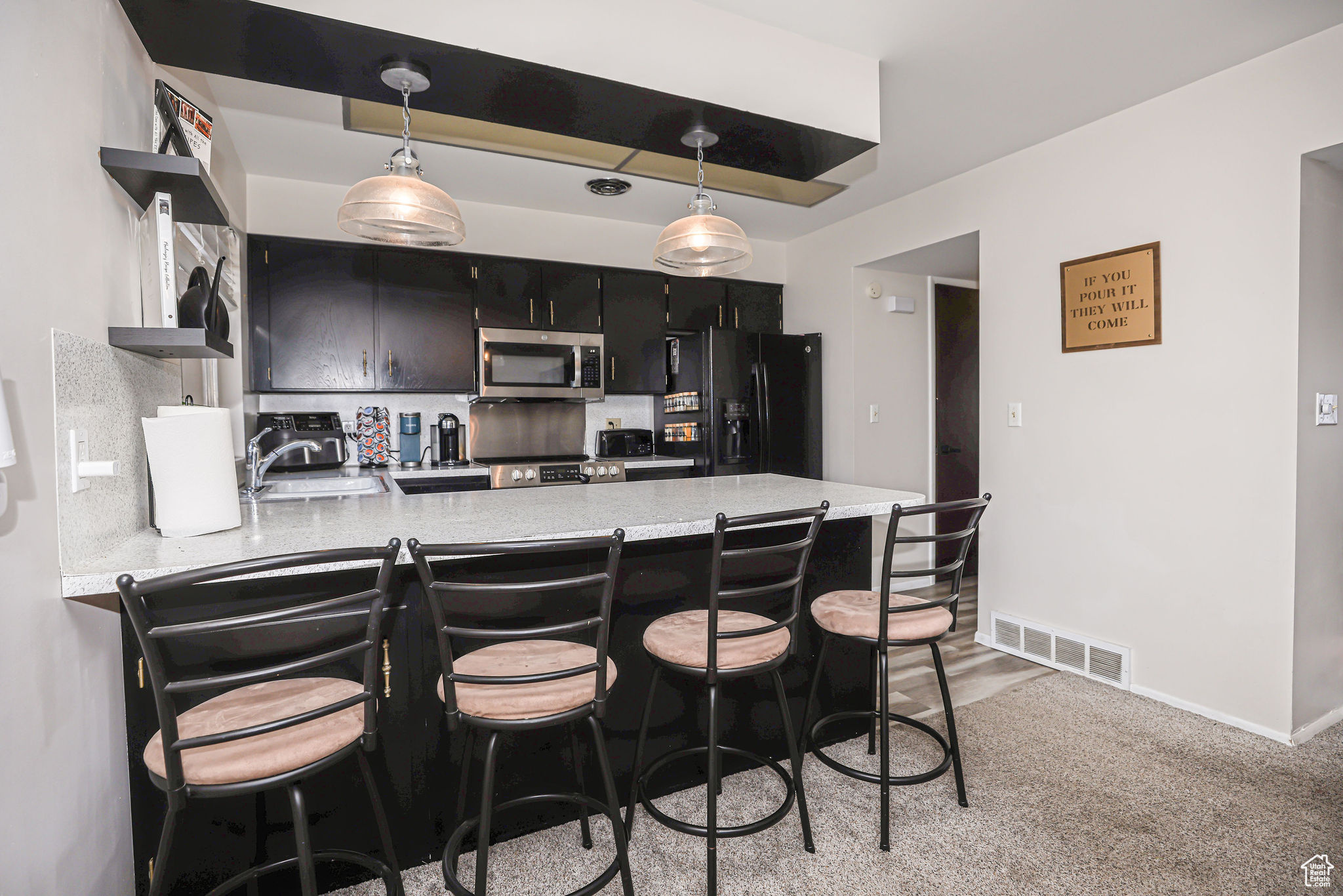 Kitchen featuring black refrigerator with ice dispenser, hanging light fixtures, sink, a kitchen bar, and kitchen peninsula