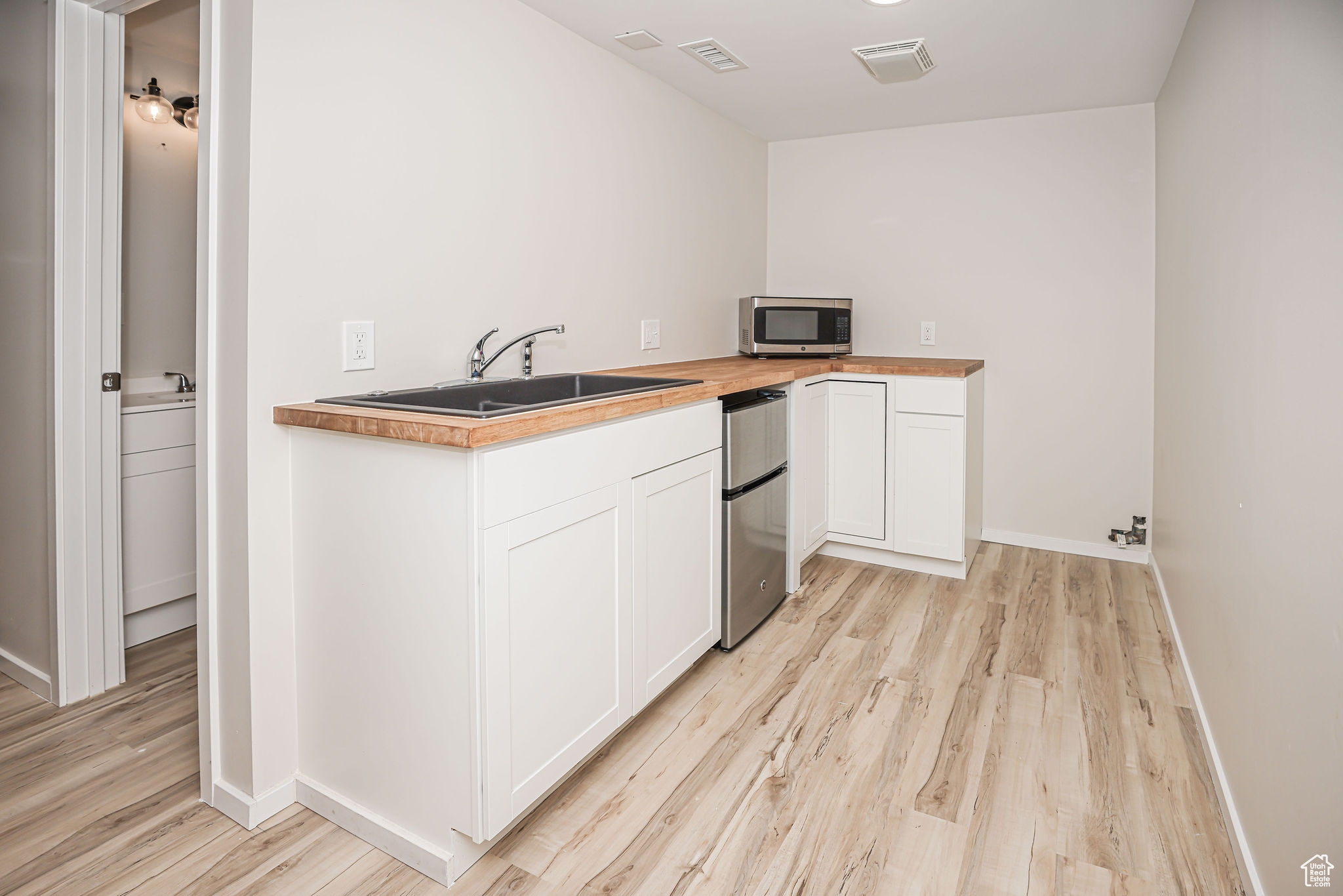 Kitchen featuring sink, butcher block countertops, light hardwood / wood-style floors, fridge, and white cabinets