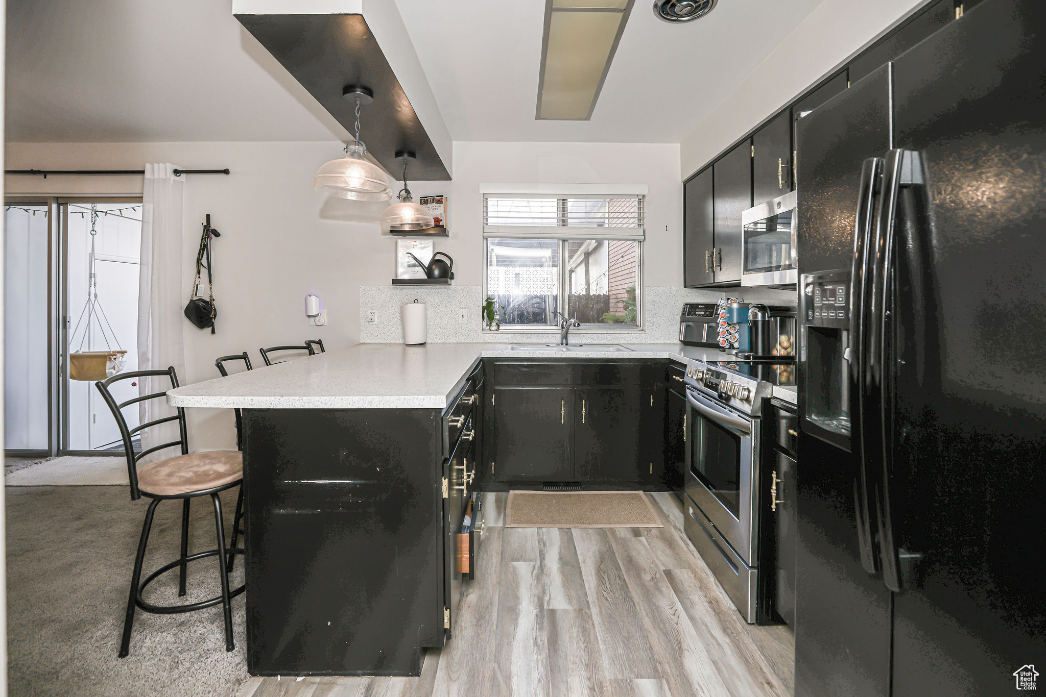 Kitchen with light hardwood / wood-style flooring, kitchen peninsula, pendant lighting, a kitchen bar, and appliances with stainless steel finishes