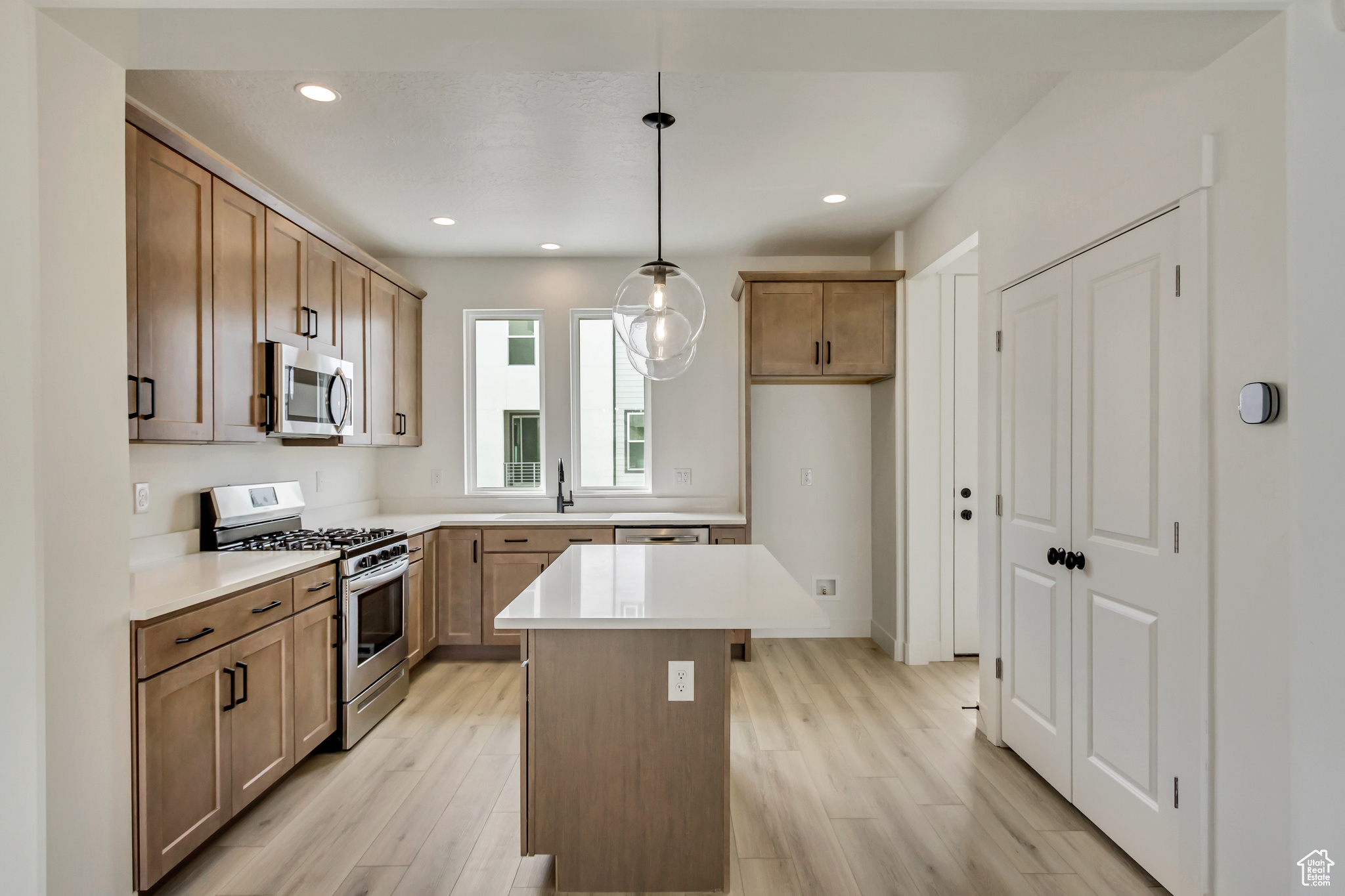 Kitchen with sink, hanging light fixtures, appliances with stainless steel finishes, a kitchen island, and light wood-type flooring