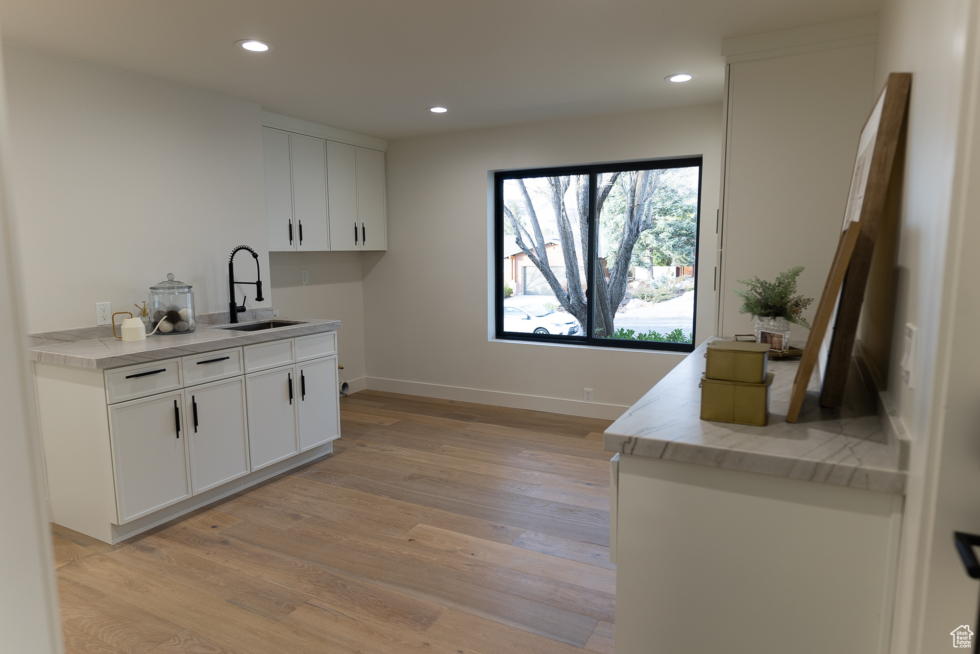 Kitchen featuring white cabinets, light wood-type flooring, light stone counters, and sink