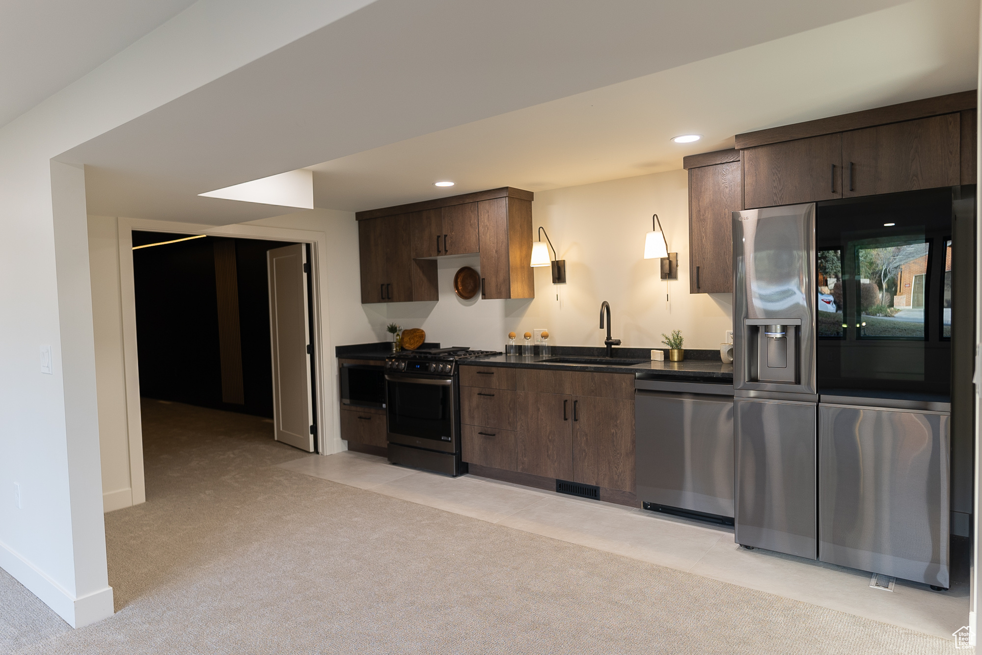 Kitchen featuring dark brown cabinetry, sink, appliances with stainless steel finishes, and light carpet