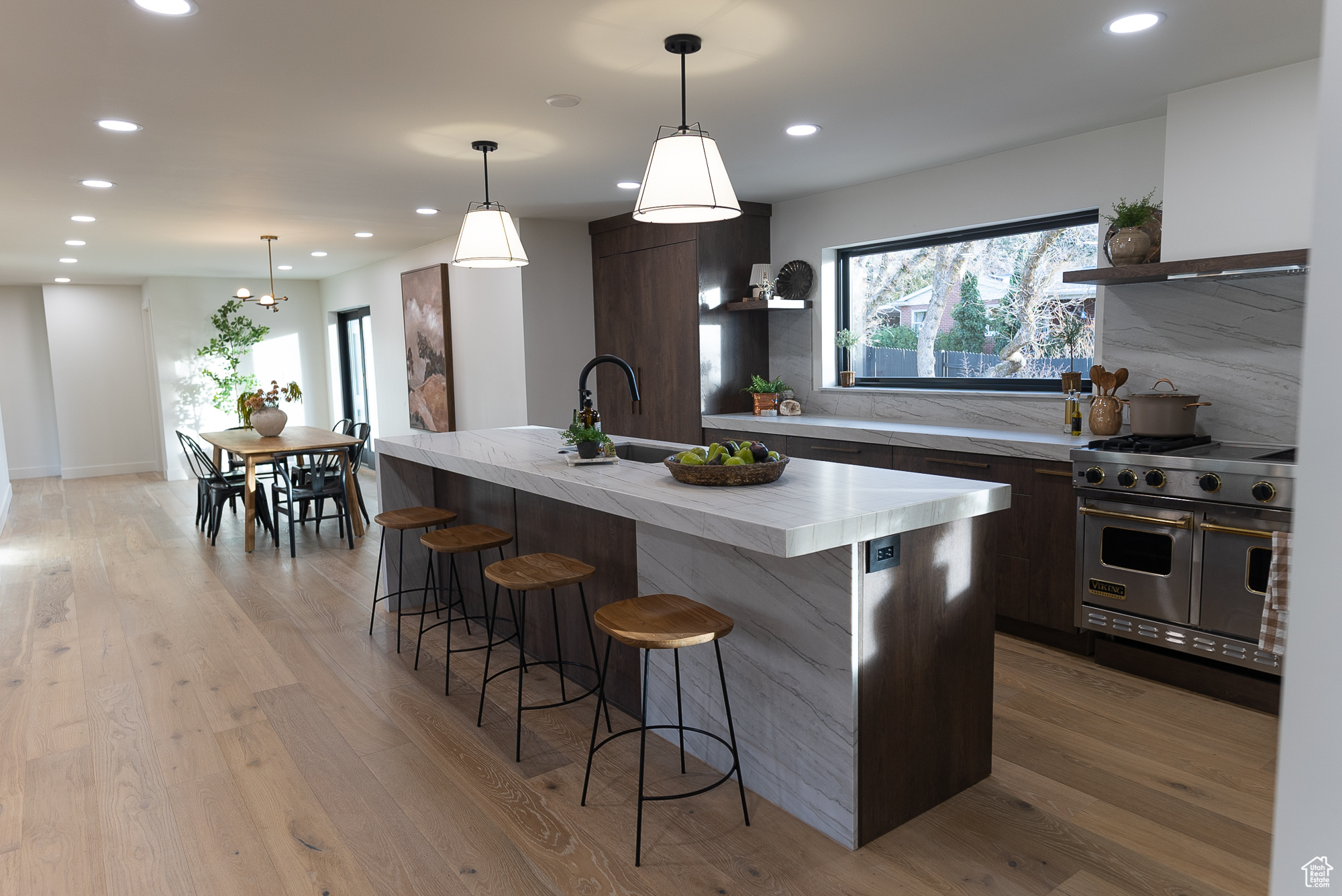 Kitchen featuring tasteful backsplash, pendant lighting, designer range, dark brown cabinets, and a center island with sink