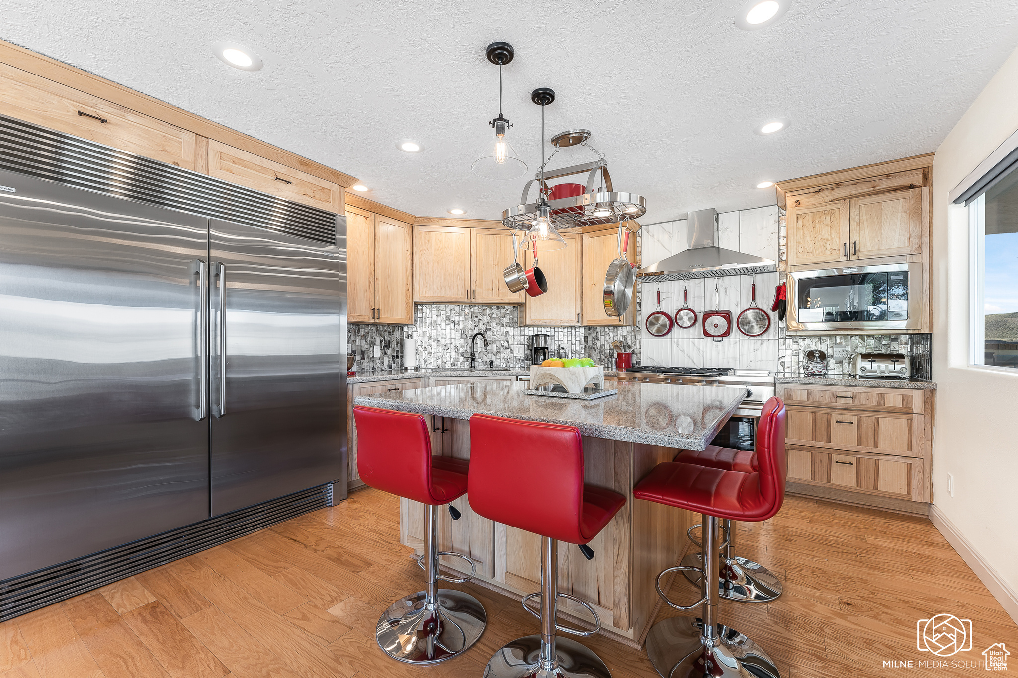 Kitchen featuring light stone counters, sink, wall chimney range hood, built in appliances, and a center island