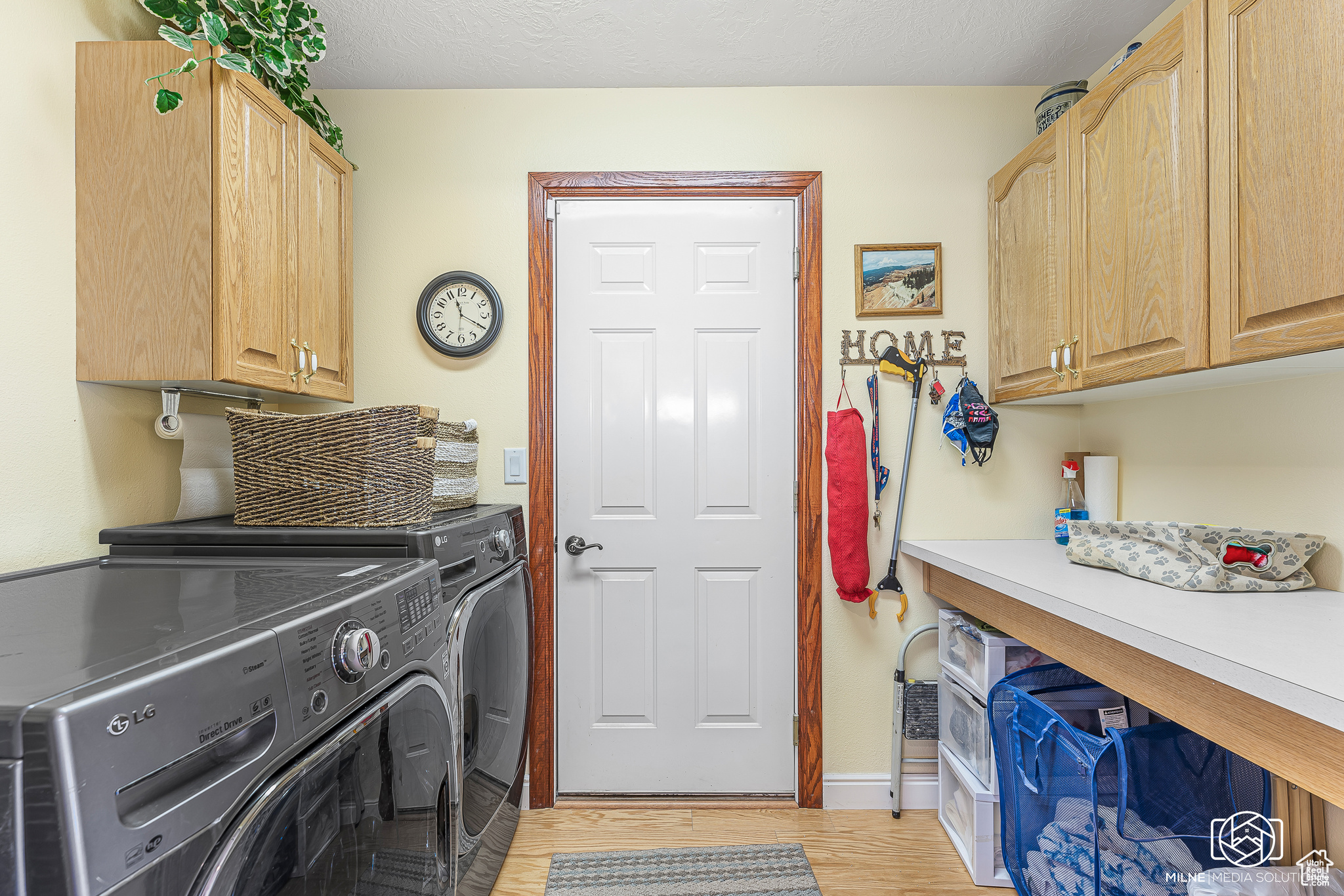 Washroom with washer and dryer, cabinets, light wood-type flooring, and a textured ceiling