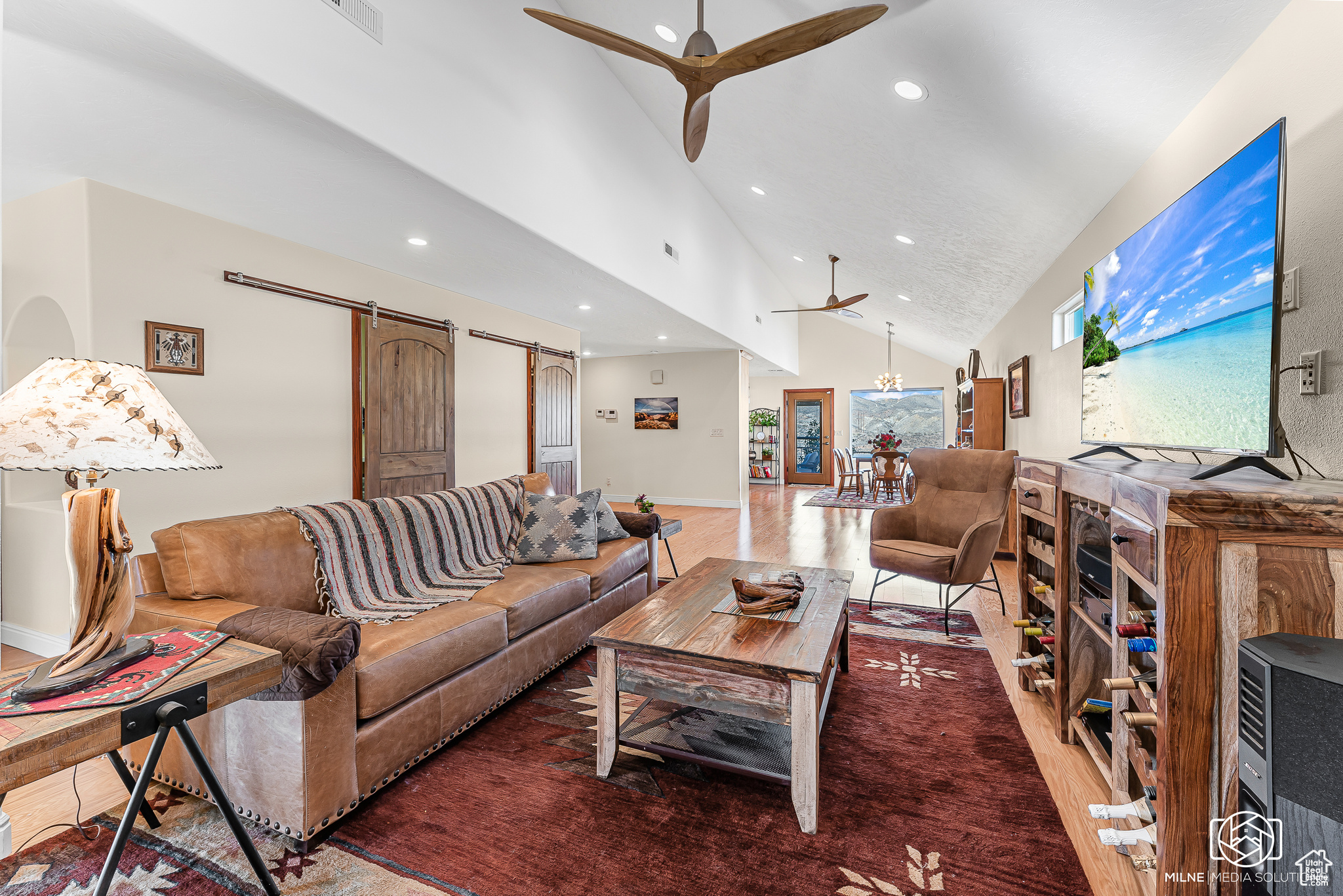 Living room featuring ceiling fan, a barn door, wood-type flooring, and high vaulted ceiling