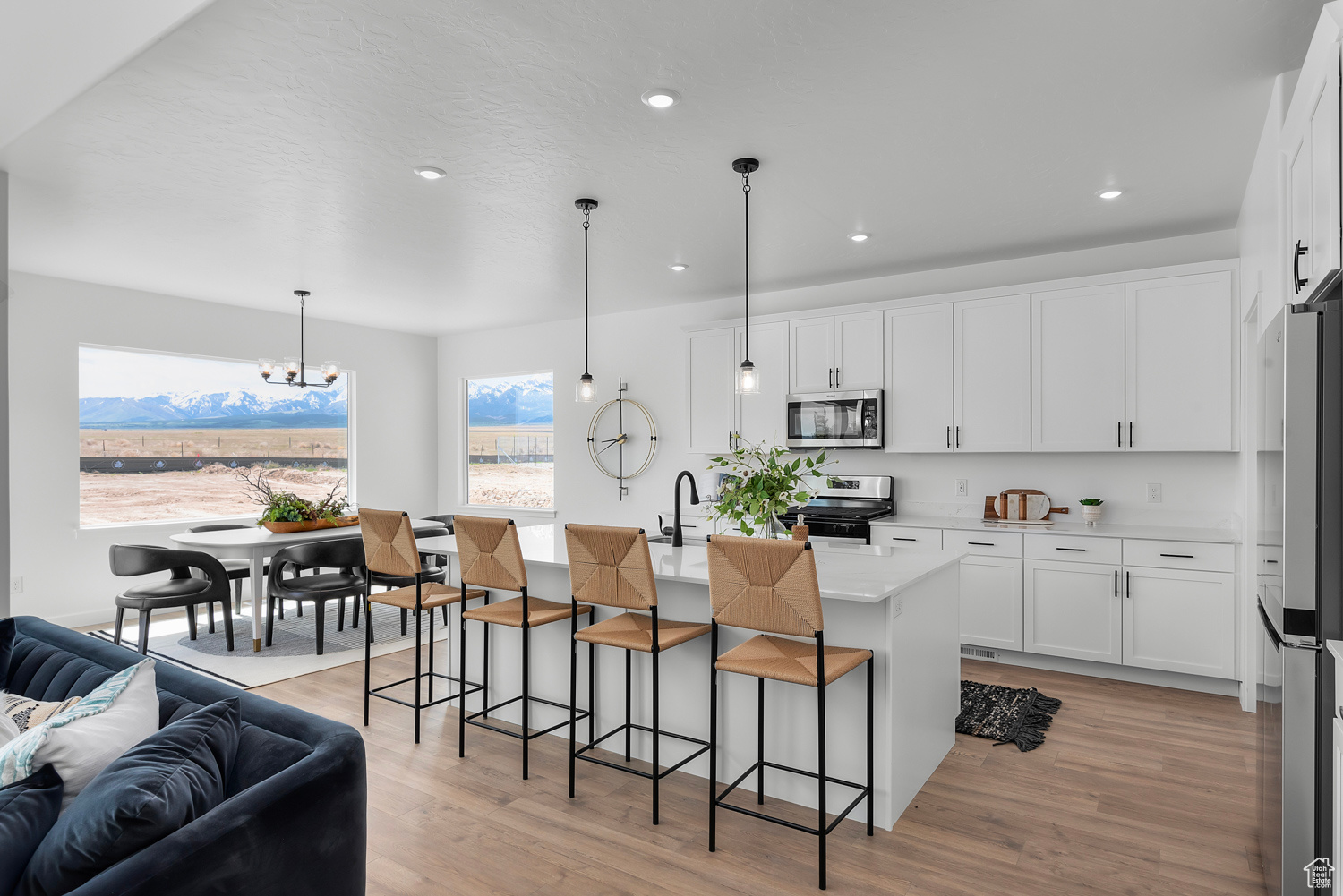 Kitchen featuring an inviting chandelier, an island with sink, decorative light fixtures, white cabinets, and appliances with stainless steel finishes