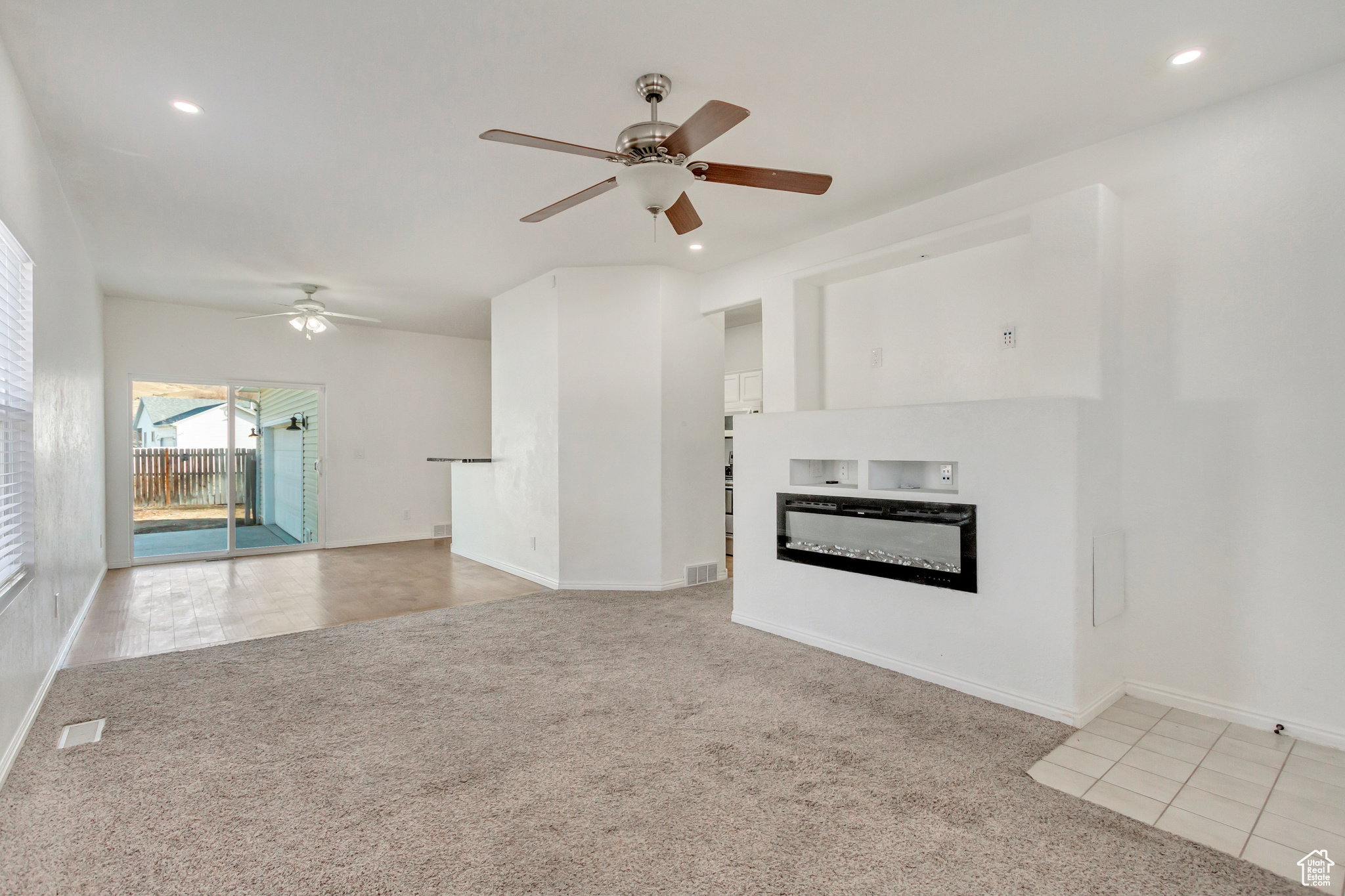 Unfurnished living room featuring light colored carpet, fireplace, and ceiling fan