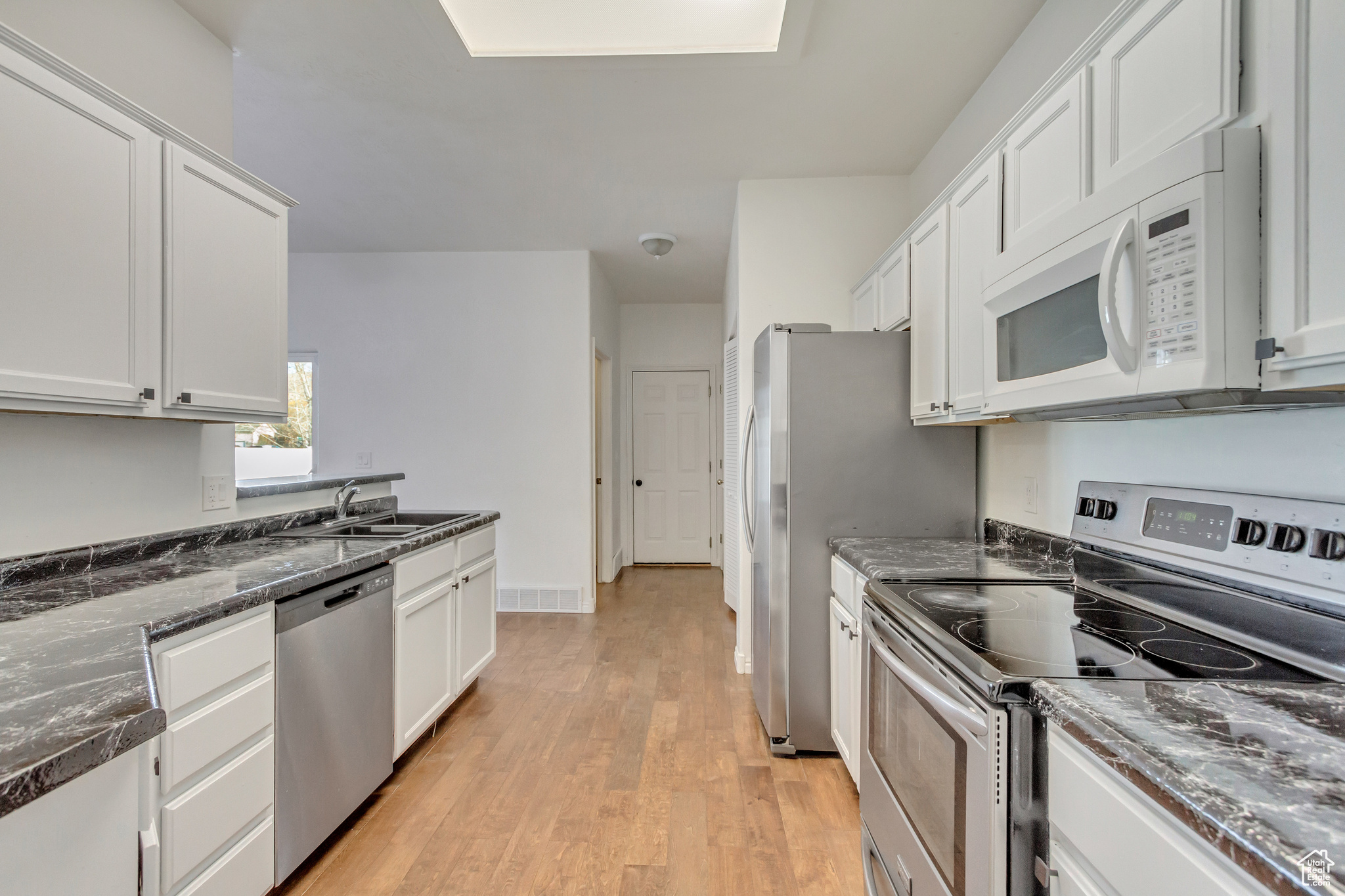 Kitchen featuring white cabinets, dark stone countertops, sink, and stainless steel appliances