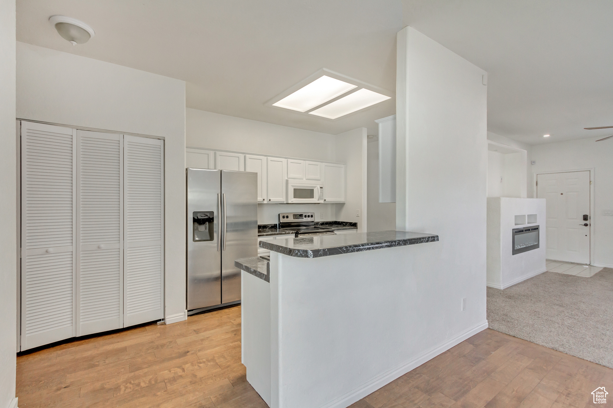 Kitchen featuring kitchen peninsula, stainless steel appliances, ceiling fan, light hardwood / wood-style flooring, and white cabinets