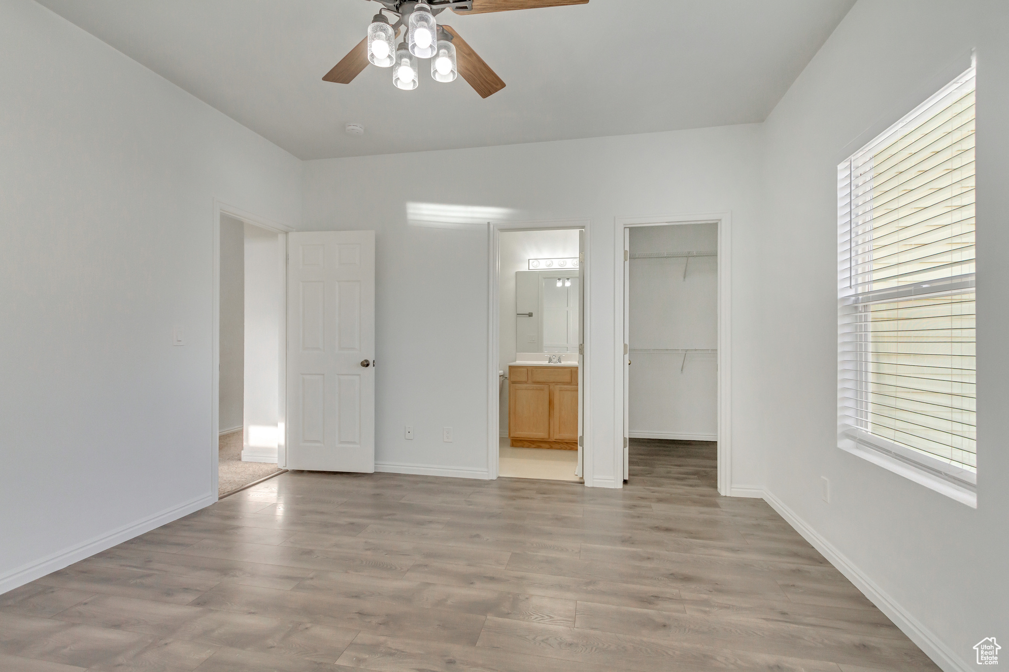 Master bedroom with ceiling fan, a walk in closet, light hardwood / wood-style flooring, and multiple windows