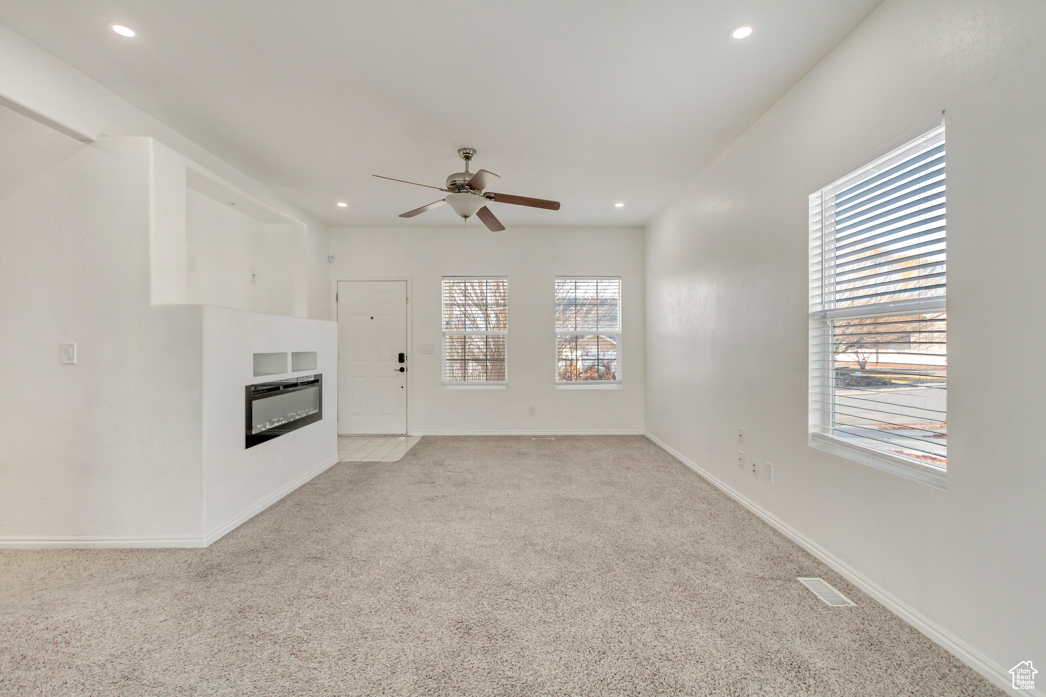 Living room with a healthy amount of sunlight, ceiling fan, fireplace, and light colored carpet