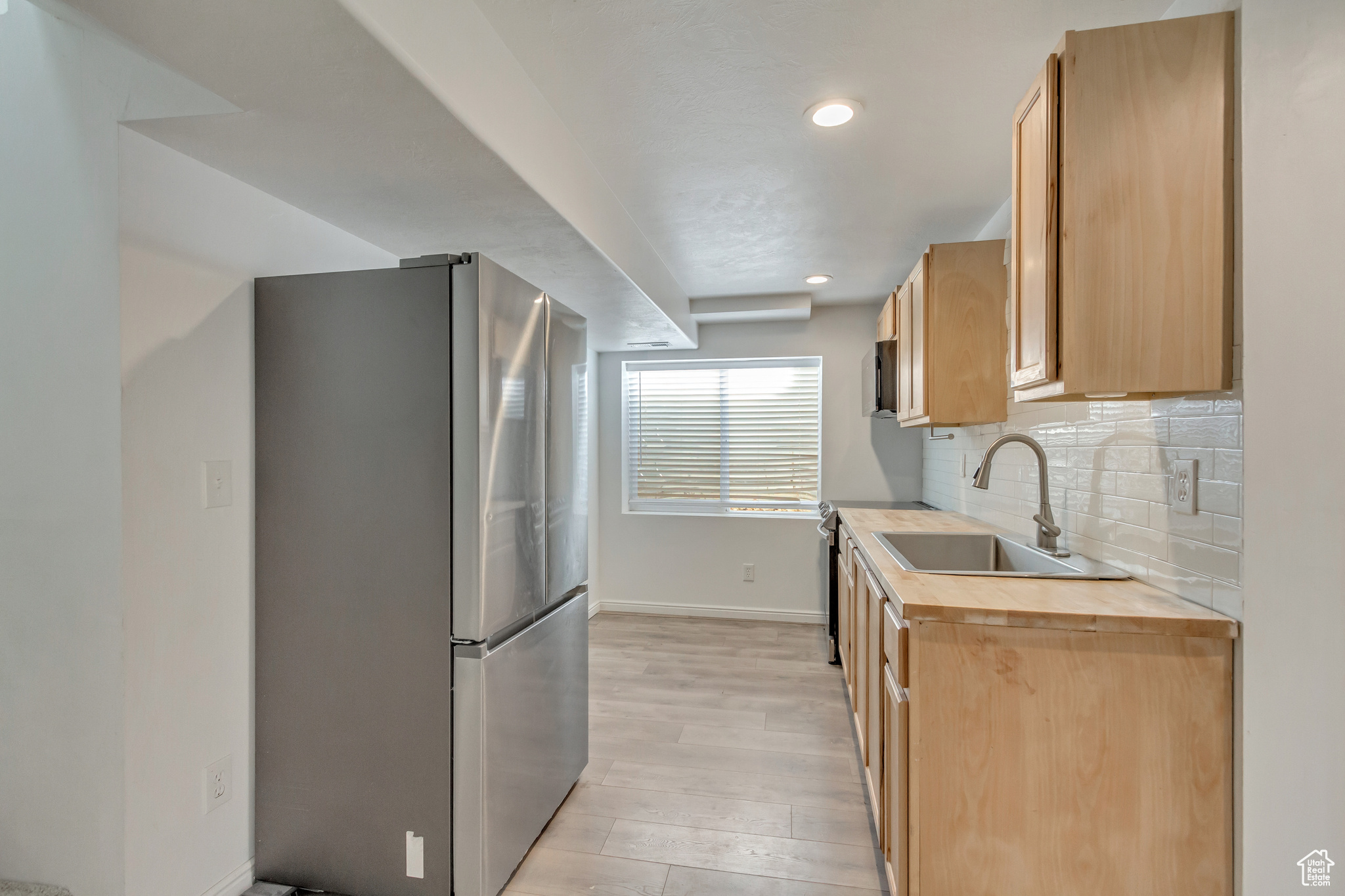 Basement Kitchen with sink, light hardwood / wood-style flooring, decorative backsplash, butcher block counters, and stainless steel refrigerator