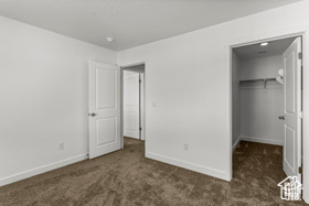 Unfurnished bedroom featuring a walk in closet, dark carpet, and a closet