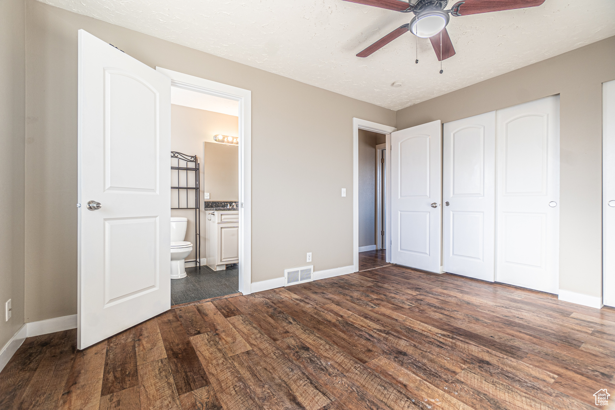 Unfurnished bedroom featuring ceiling fan, a closet, dark wood-type flooring, and ensuite bath