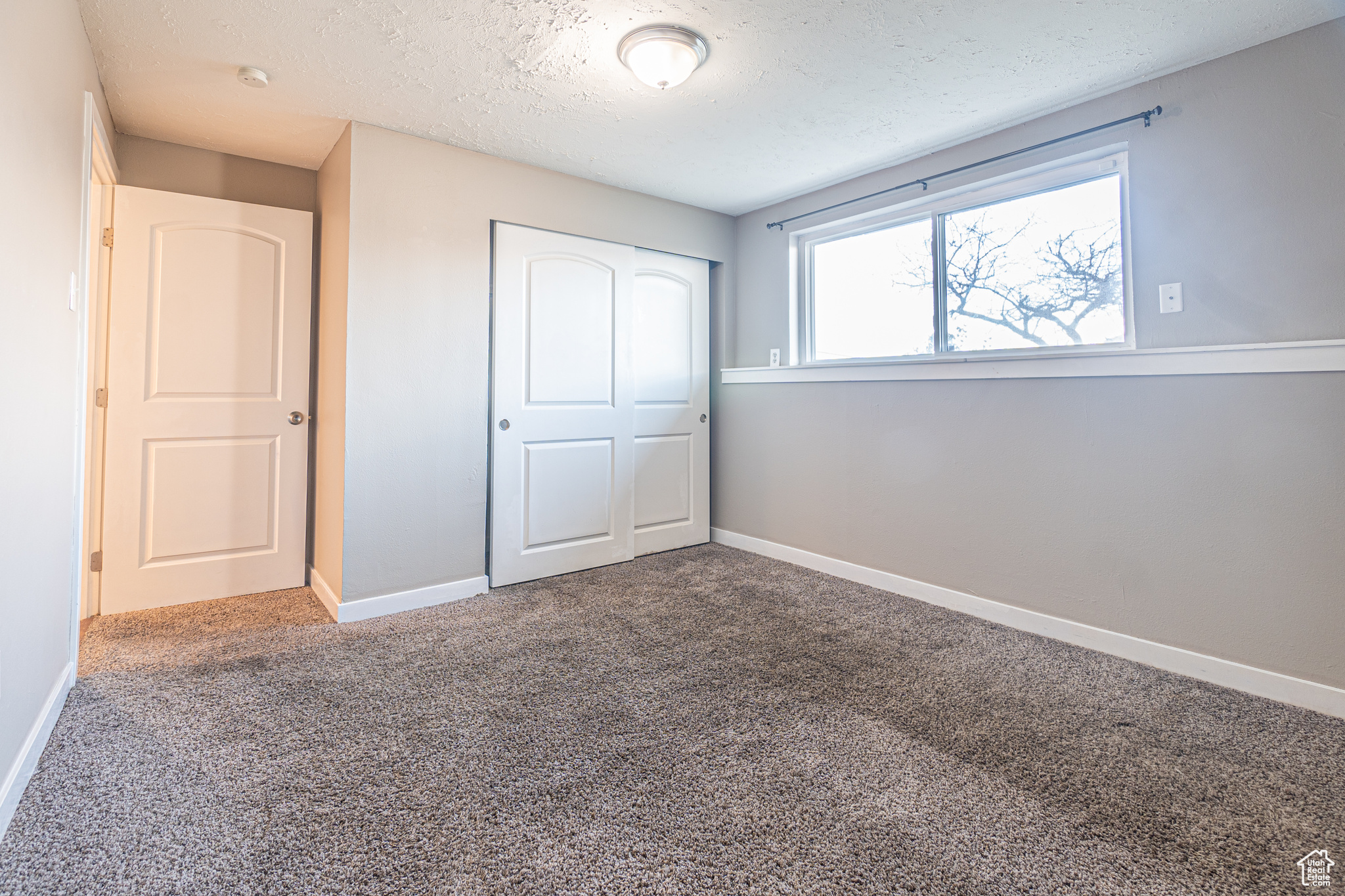 Unfurnished bedroom featuring carpet flooring, a textured ceiling, and a closet