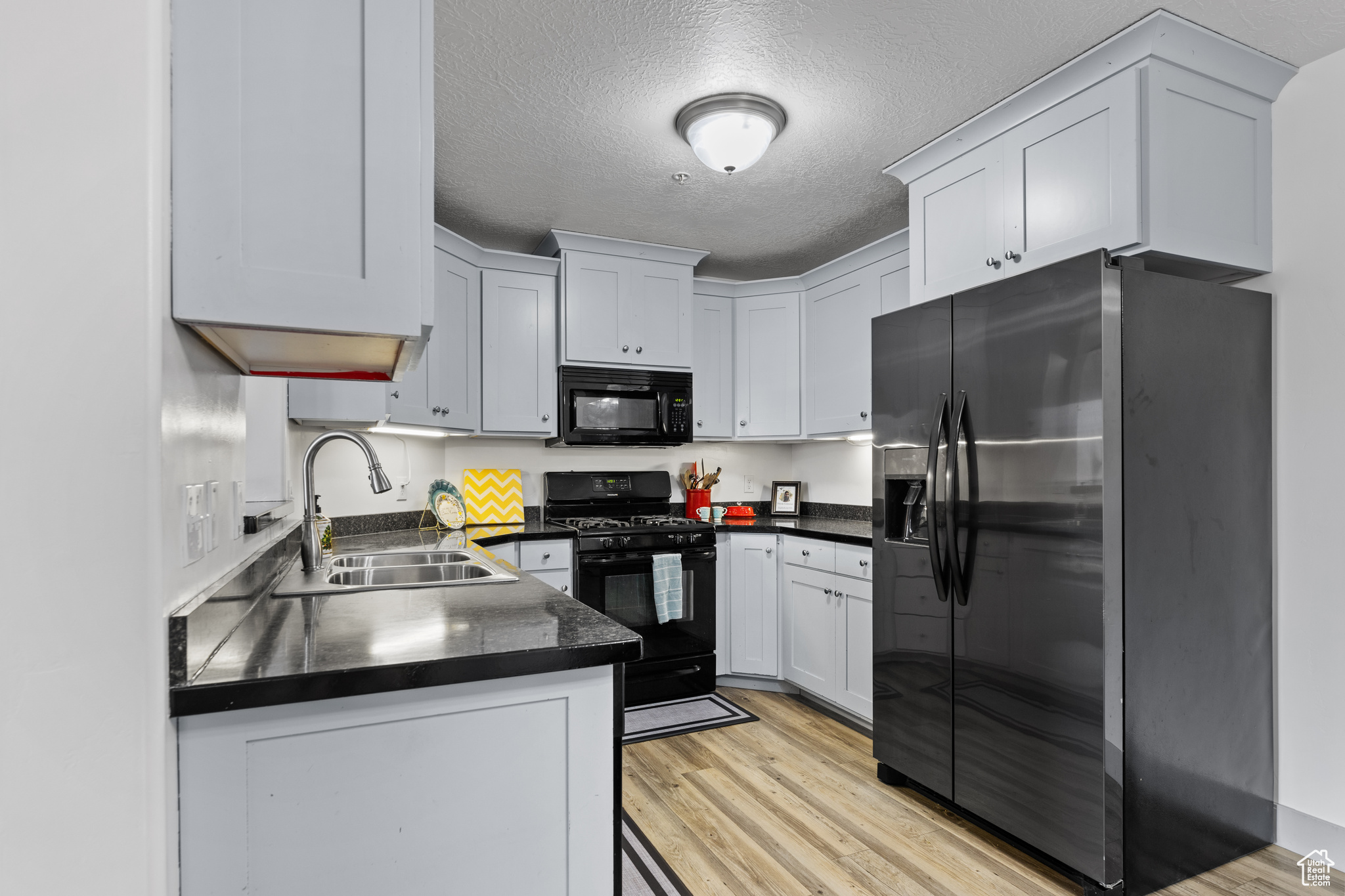 Kitchen with a textured ceiling, sink, black appliances, light hardwood / wood-style flooring, and white cabinets