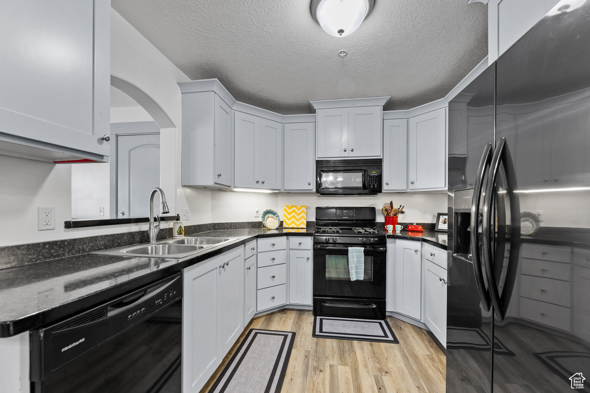 Kitchen with black appliances, white cabinets, sink, and a textured ceiling