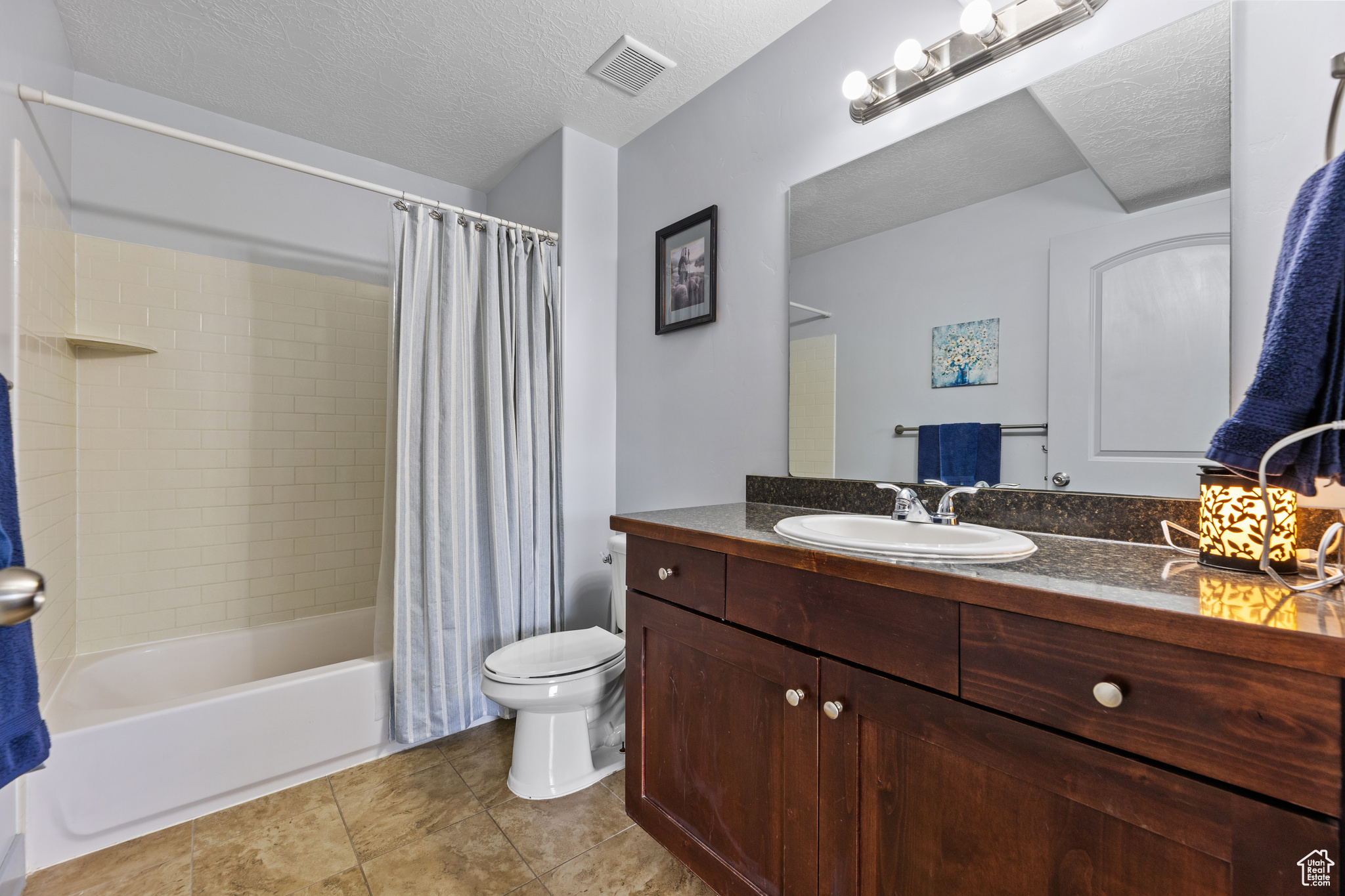 Full bathroom with vanity, shower / tub combo, a textured ceiling, and toilet