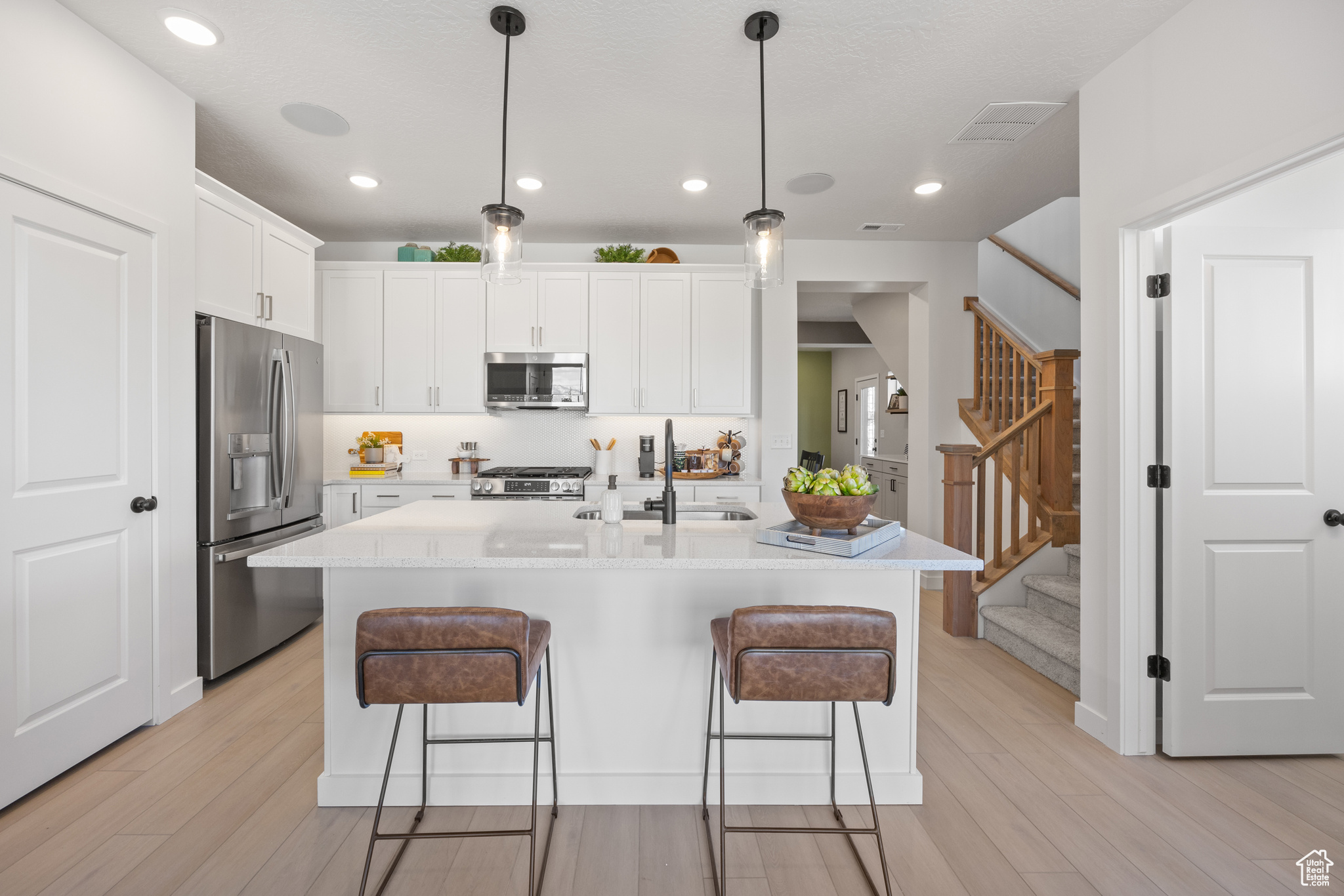 Kitchen with stainless steel appliances, sink, pendant lighting, a center island with sink, and white cabinets