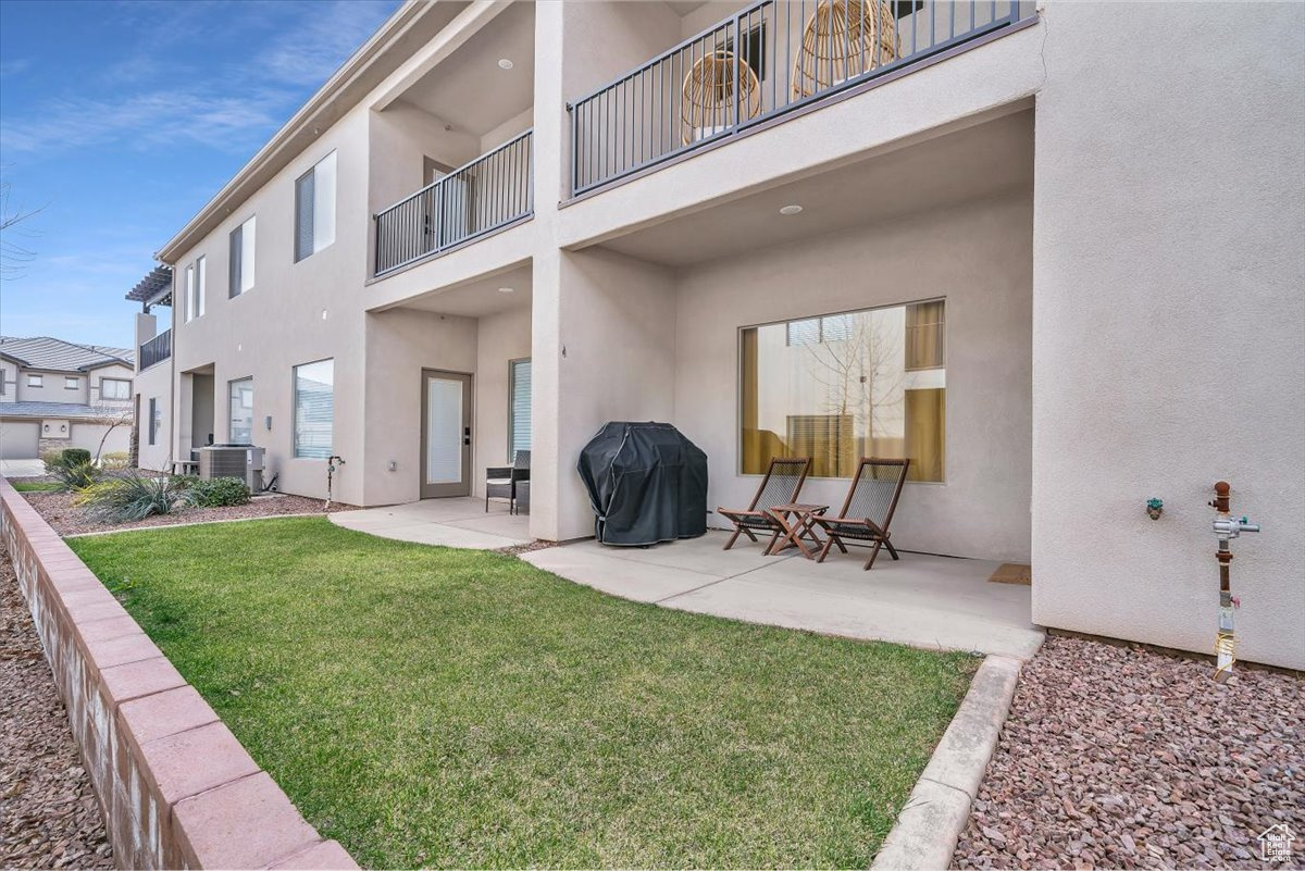 Rear view of property with a lawn, a patio area, a balcony, and central AC