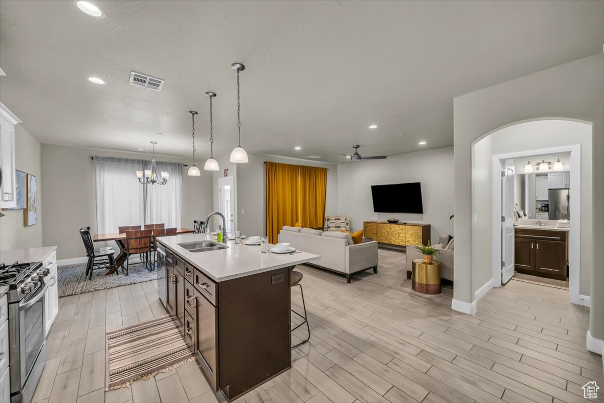 Kitchen with dark brown cabinetry, ceiling fan with notable chandelier, stainless steel appliances, a kitchen island with sink, and sink