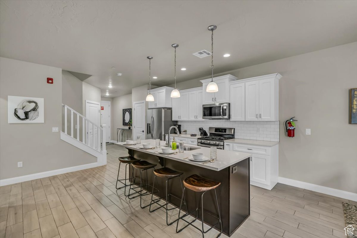 Kitchen featuring a kitchen bar, white cabinets, an island with sink, and appliances with stainless steel finishes