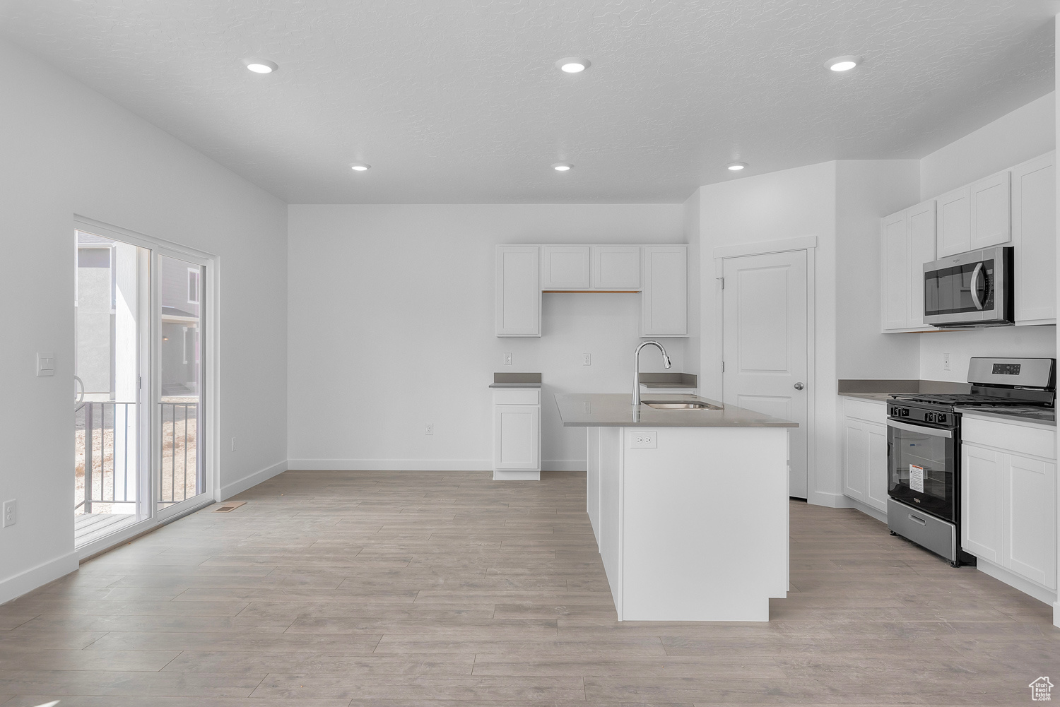 Kitchen with white cabinetry, a kitchen island with sink, light hardwood / wood-style flooring, and appliances with stainless steel finishes