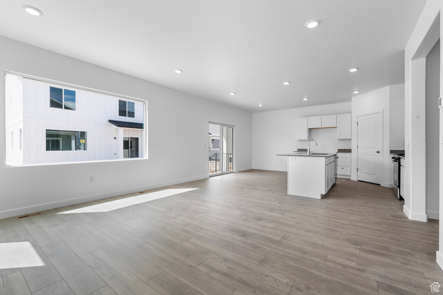 Kitchen featuring a center island with sink, sink, light hardwood / wood-style floors, white cabinetry, and stainless steel range with gas stovetop