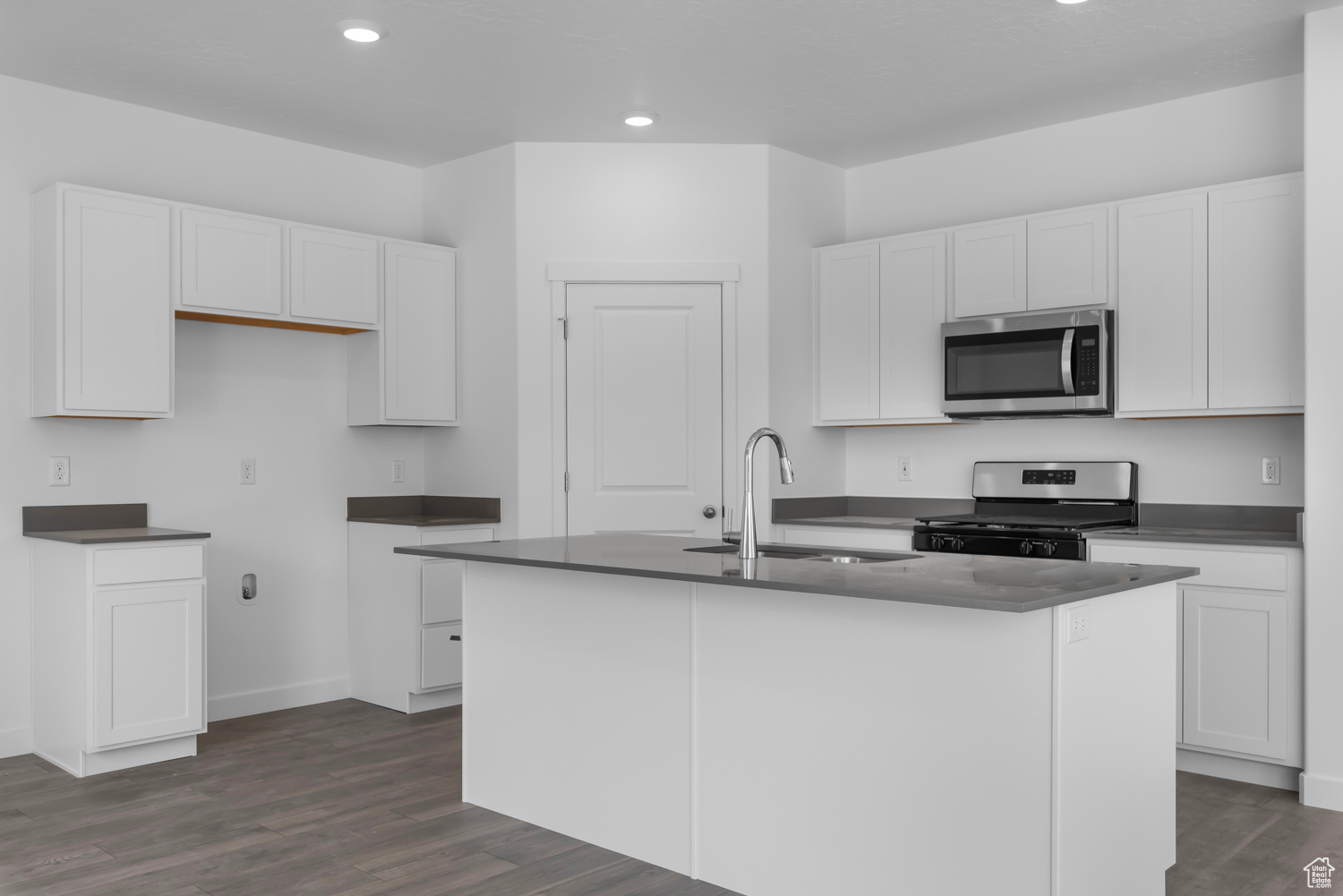 Kitchen featuring dark hardwood / wood-style flooring, stainless steel appliances, a kitchen island with sink, sink, and white cabinets