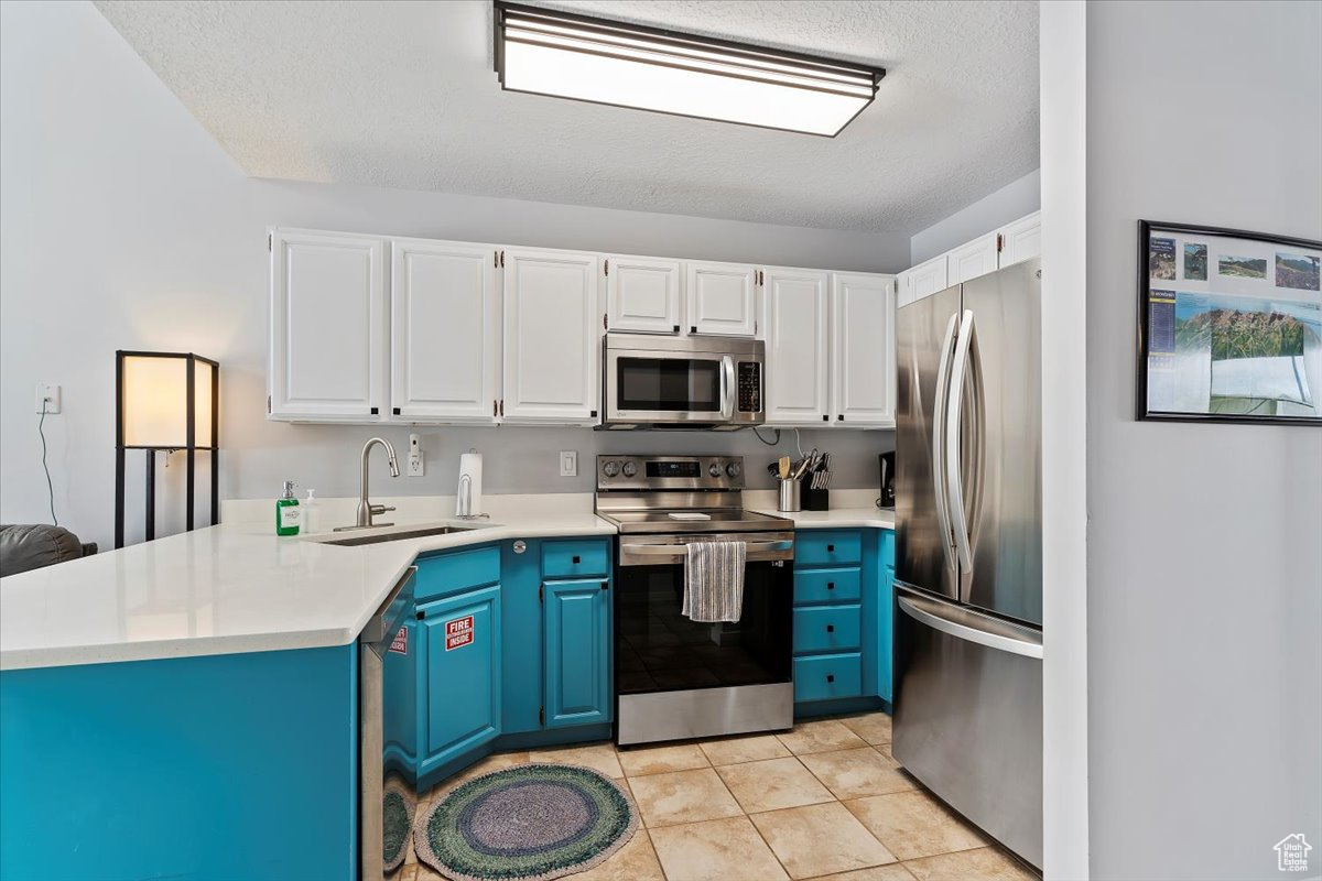 Kitchen with white cabinets, sink, blue cabinetry, light tile patterned flooring, and stainless steel appliances