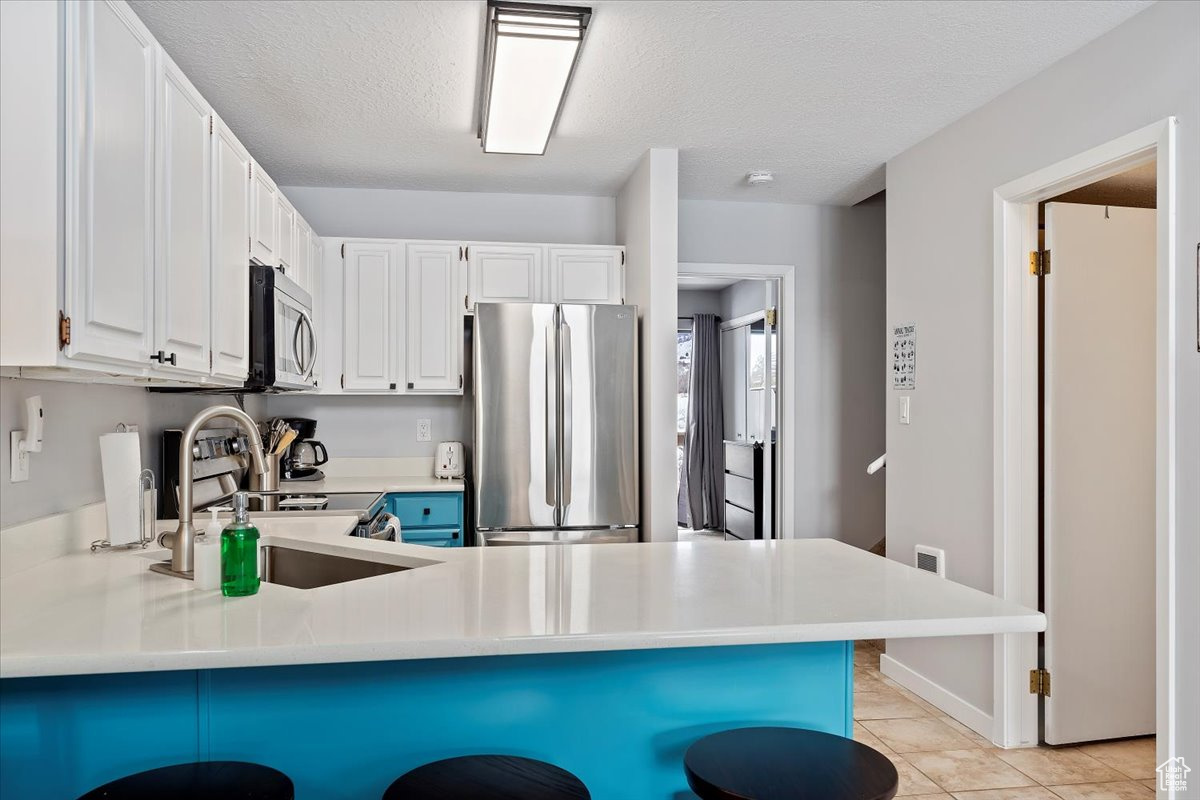 Kitchen with appliances with stainless steel finishes, sink, white cabinetry, a breakfast bar area, and light tile patterned flooring