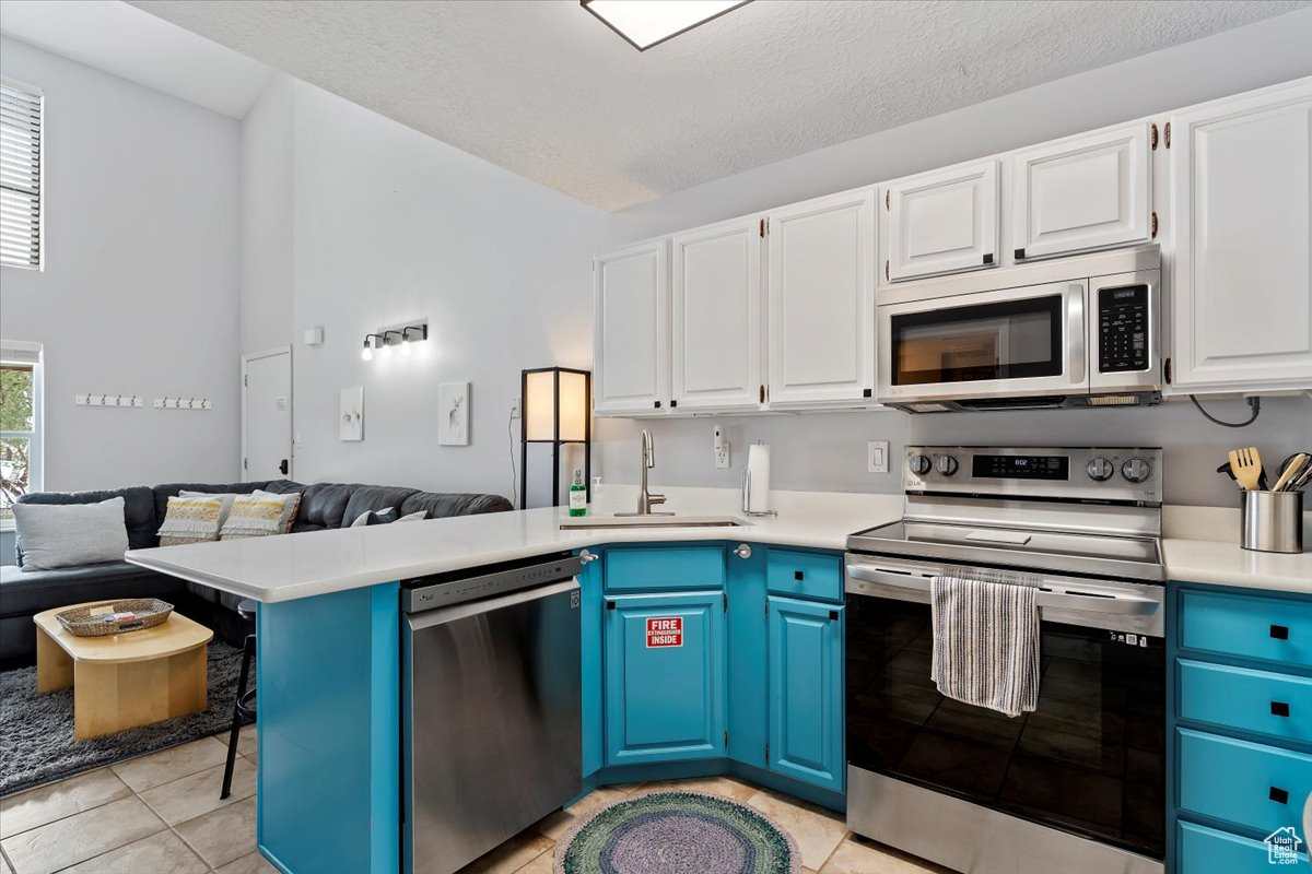 Kitchen featuring appliances with stainless steel finishes, blue cabinets, sink, white cabinets, and plenty of natural light