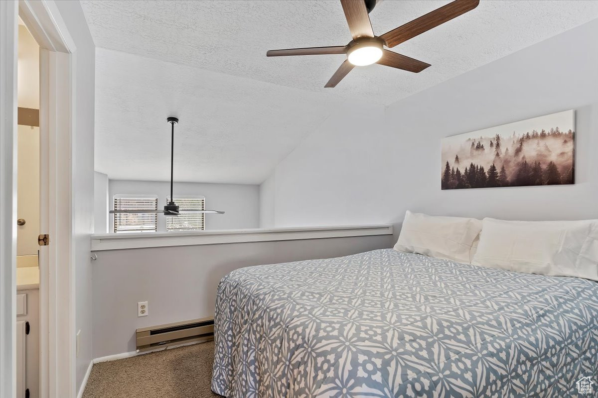 Bedroom featuring carpet flooring, ceiling fan, a baseboard heating unit, a textured ceiling, and vaulted ceiling