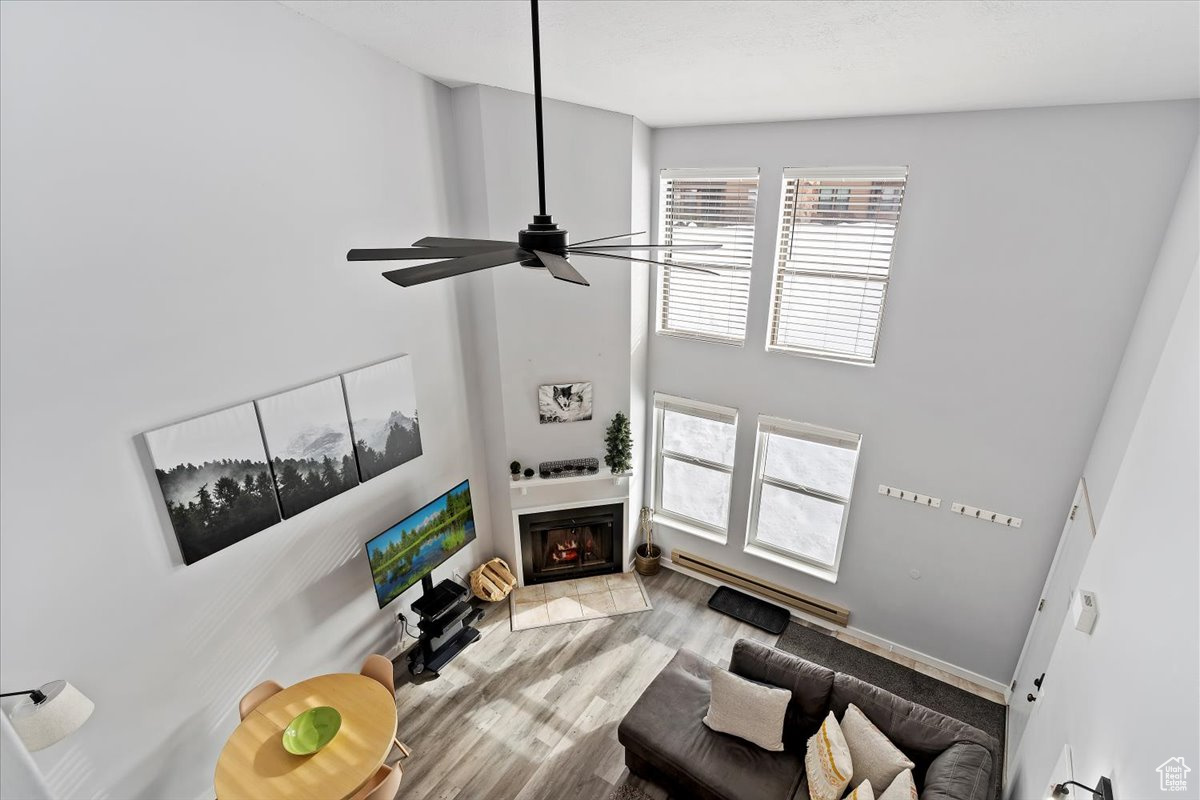 Living room with ceiling fan, light hardwood / wood-style floors, a towering ceiling, and a baseboard radiator