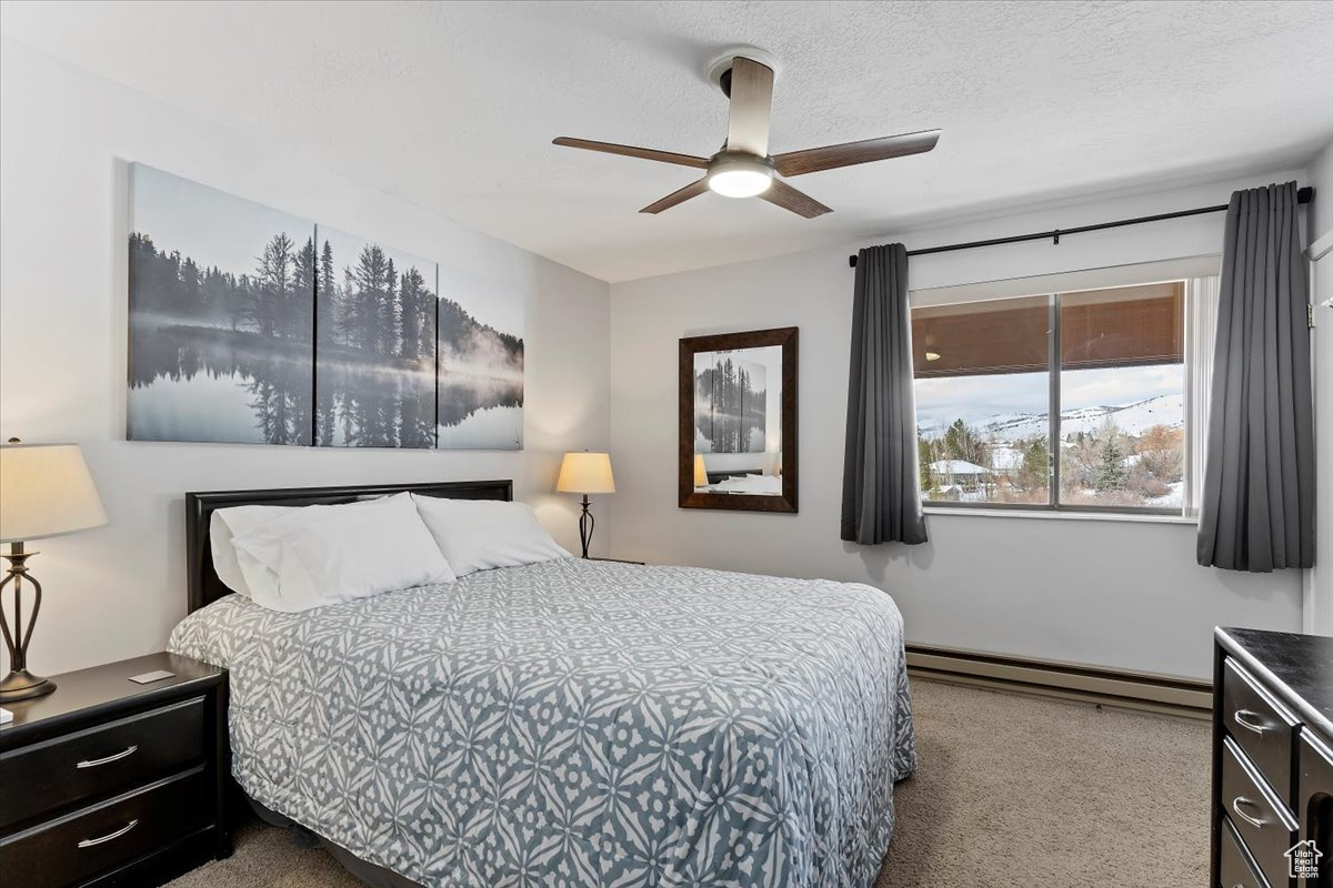 Carpeted bedroom featuring ceiling fan, a textured ceiling, and a baseboard heating unit